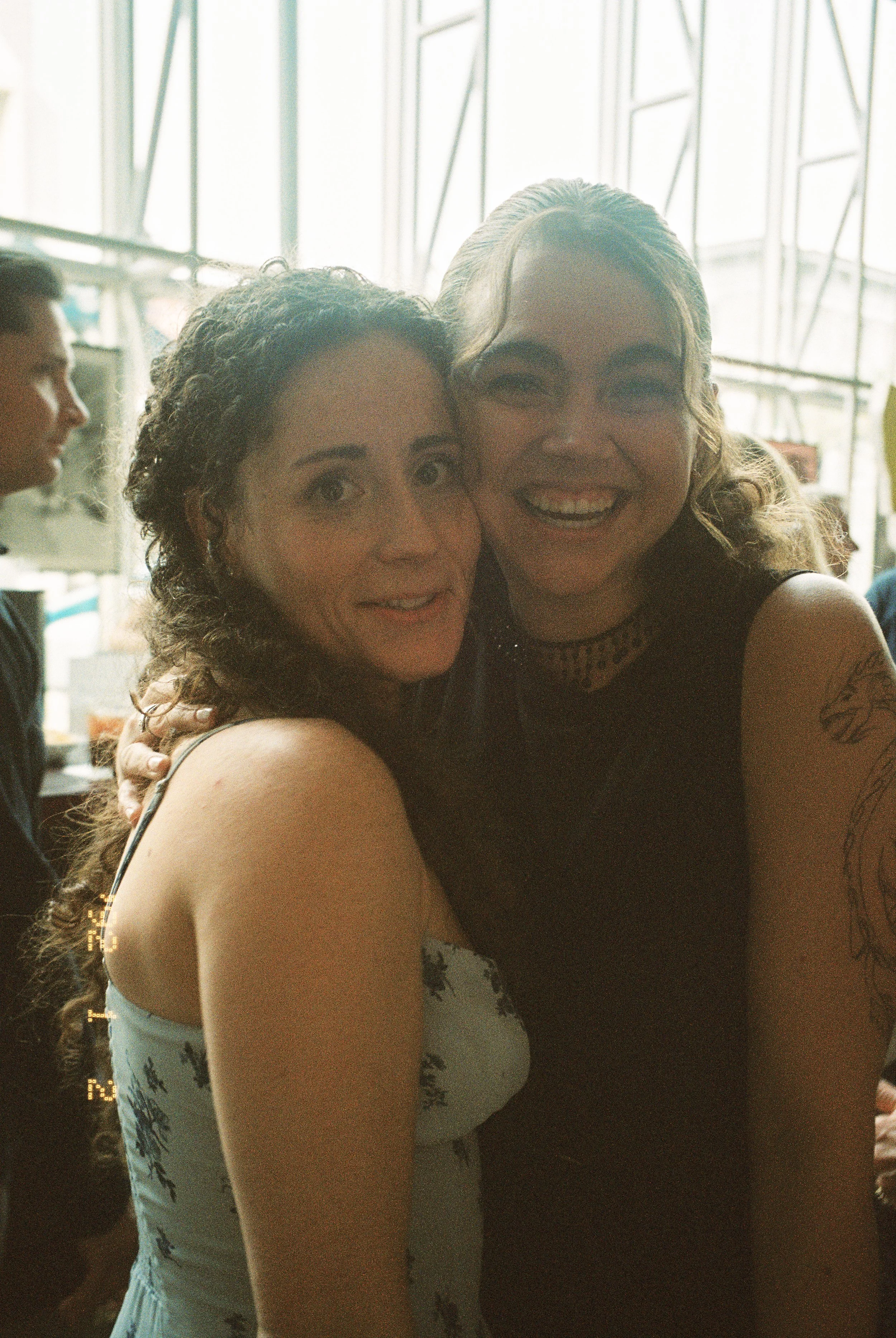 Two women hugging and smiling together during a wedding rehearsal dinner gathering.