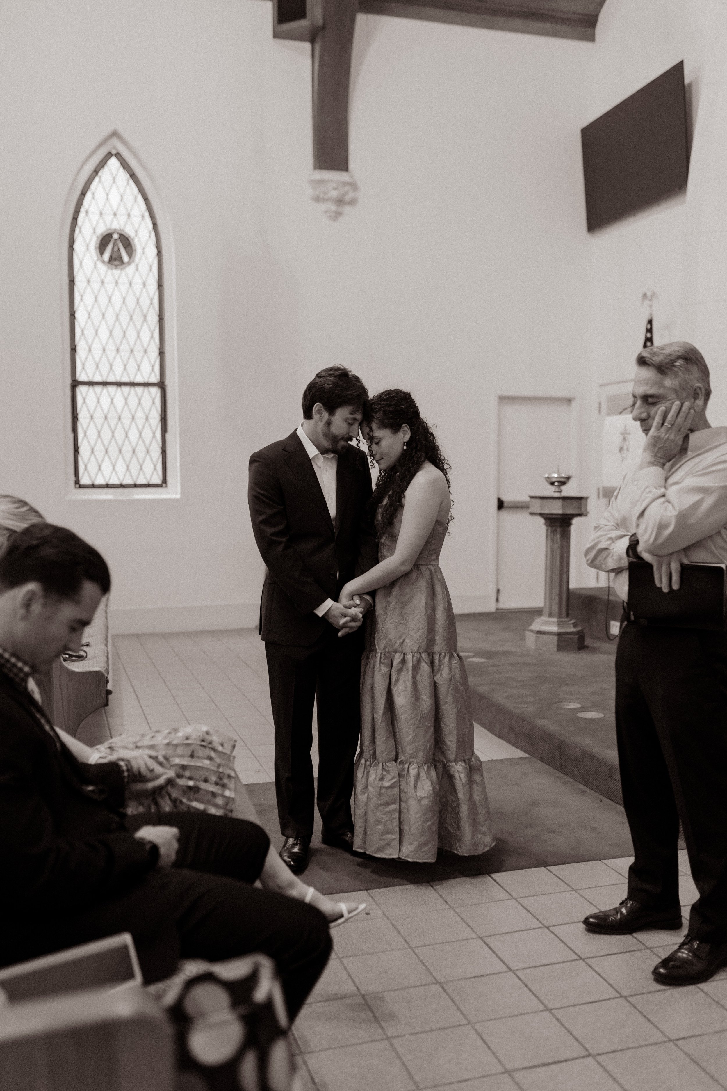Couple holding hands during an intimate moment at their wedding rehearsal inside a church.