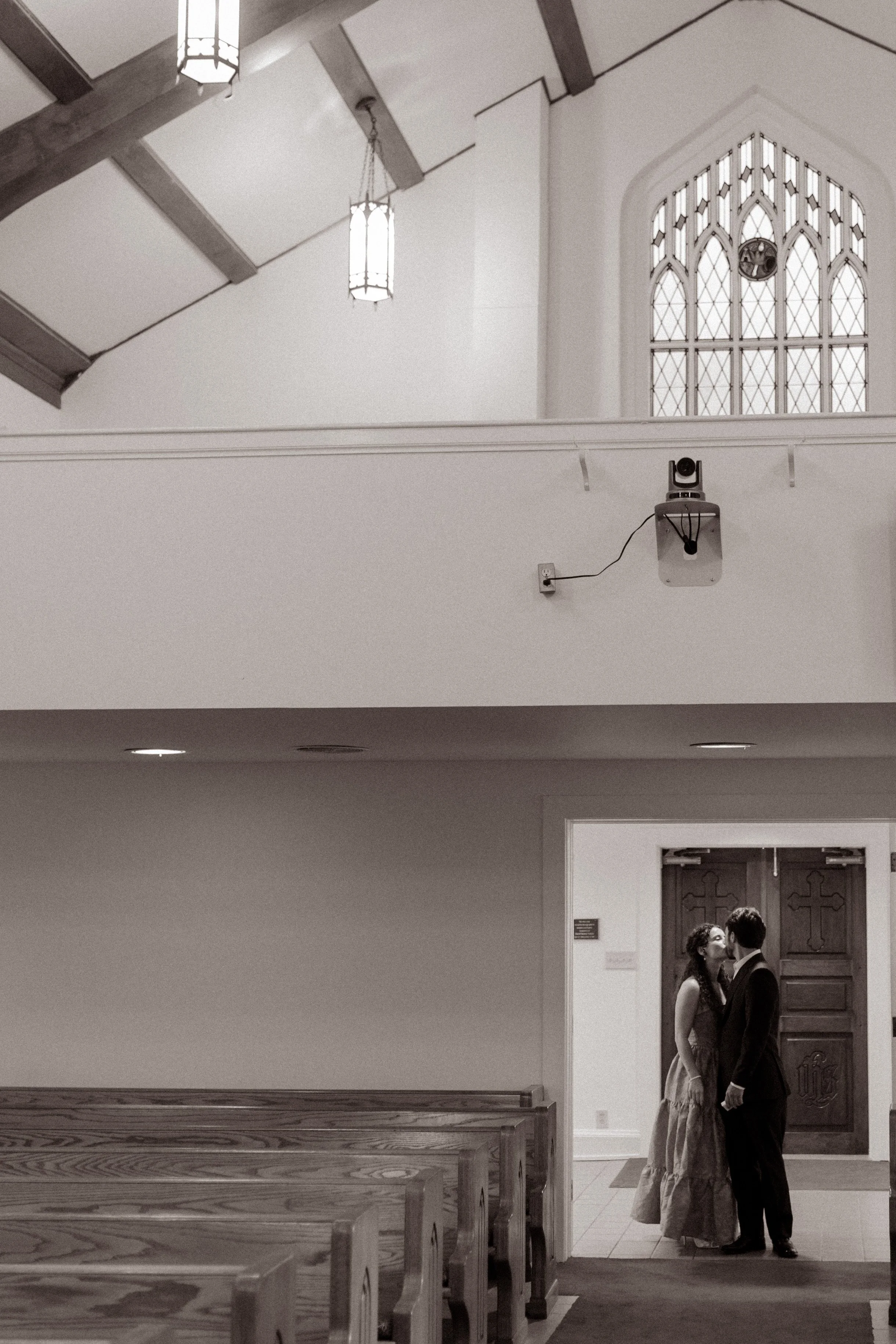 Black-and-white photo of a couple sharing a kiss in the doorway of a quiet church.