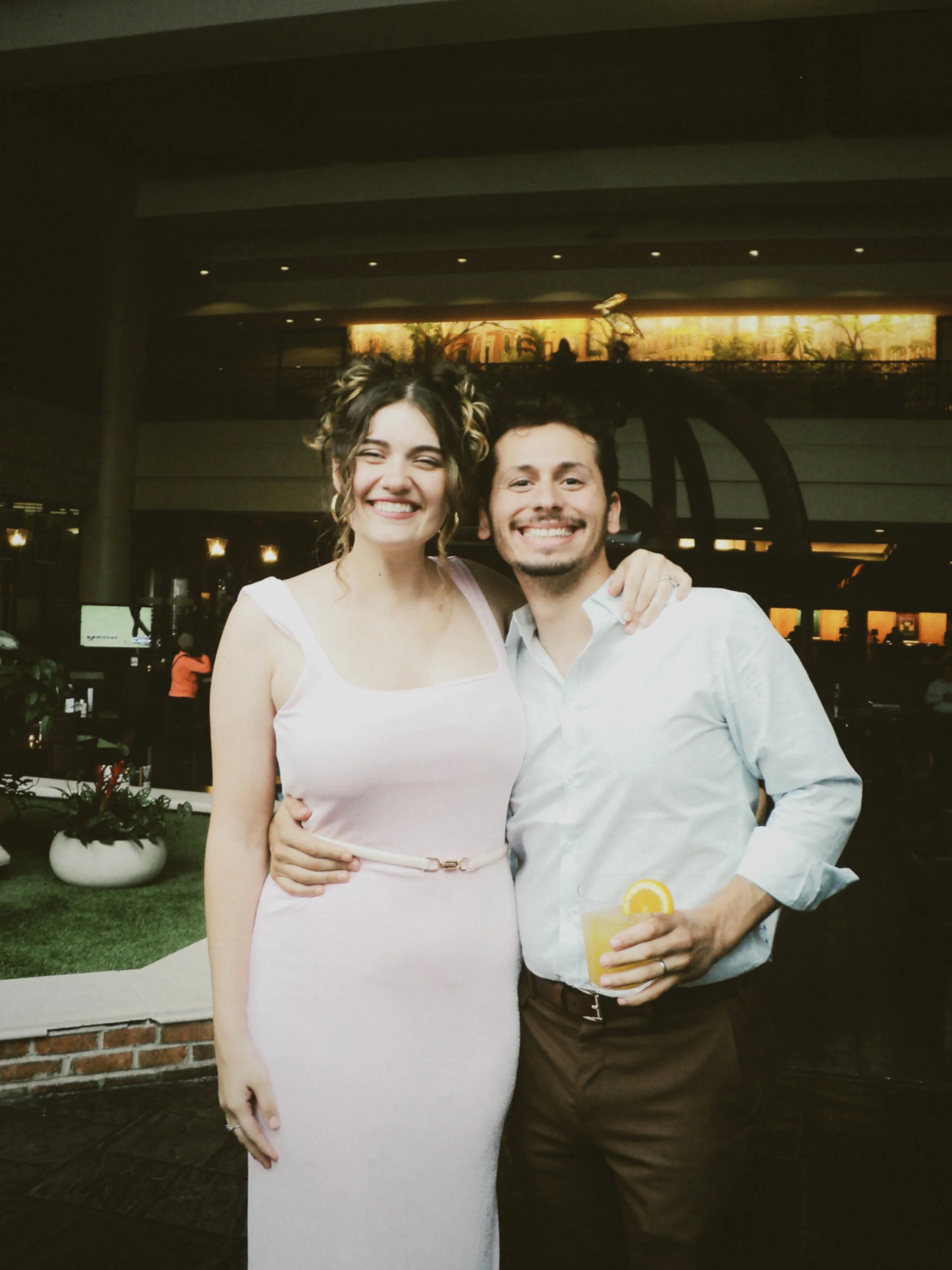 Smiling couple posing together with a drink during the wedding rehearsal dinner celebration.