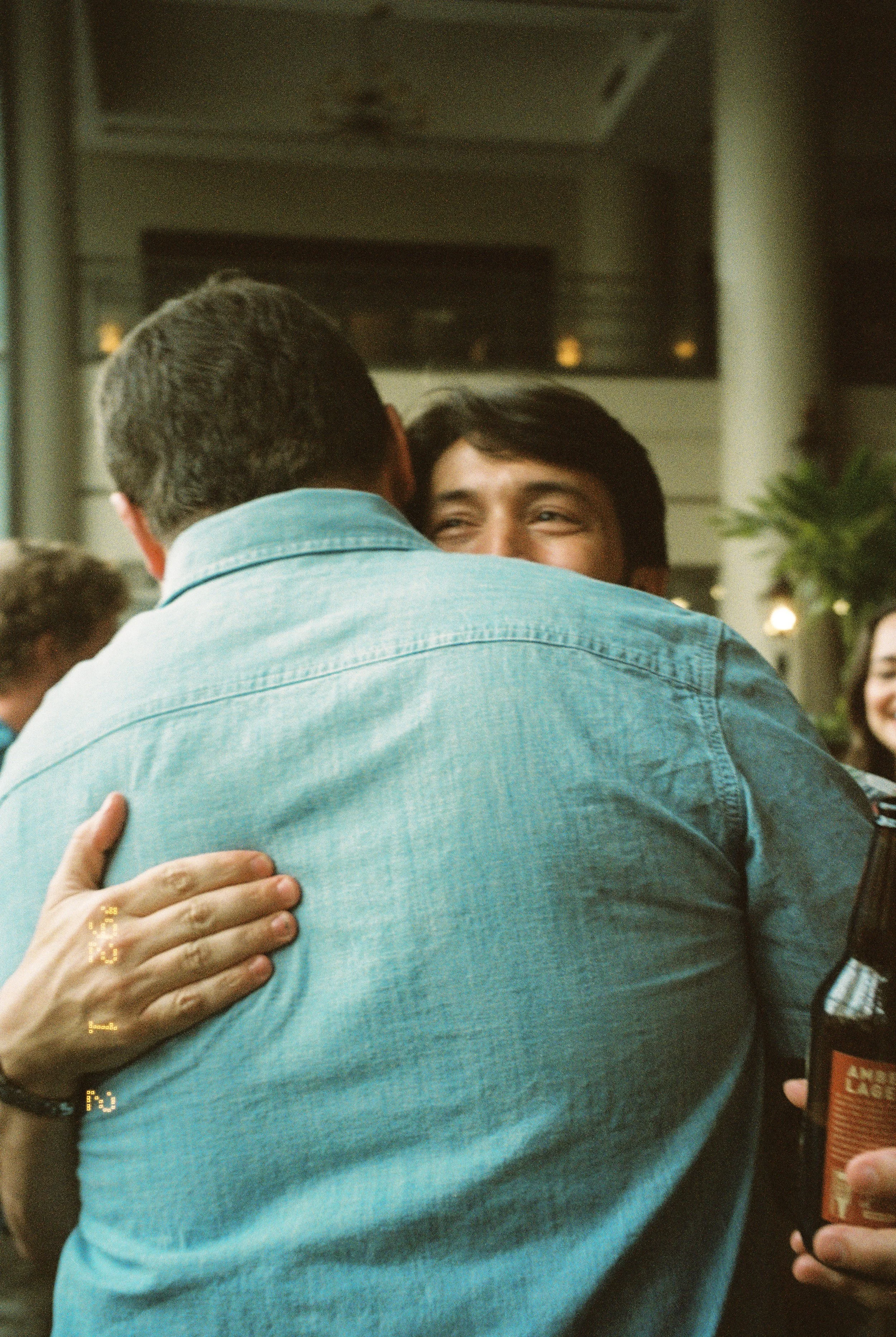 Two guests greeting each other with a warm hug during the wedding rehearsal dinner.