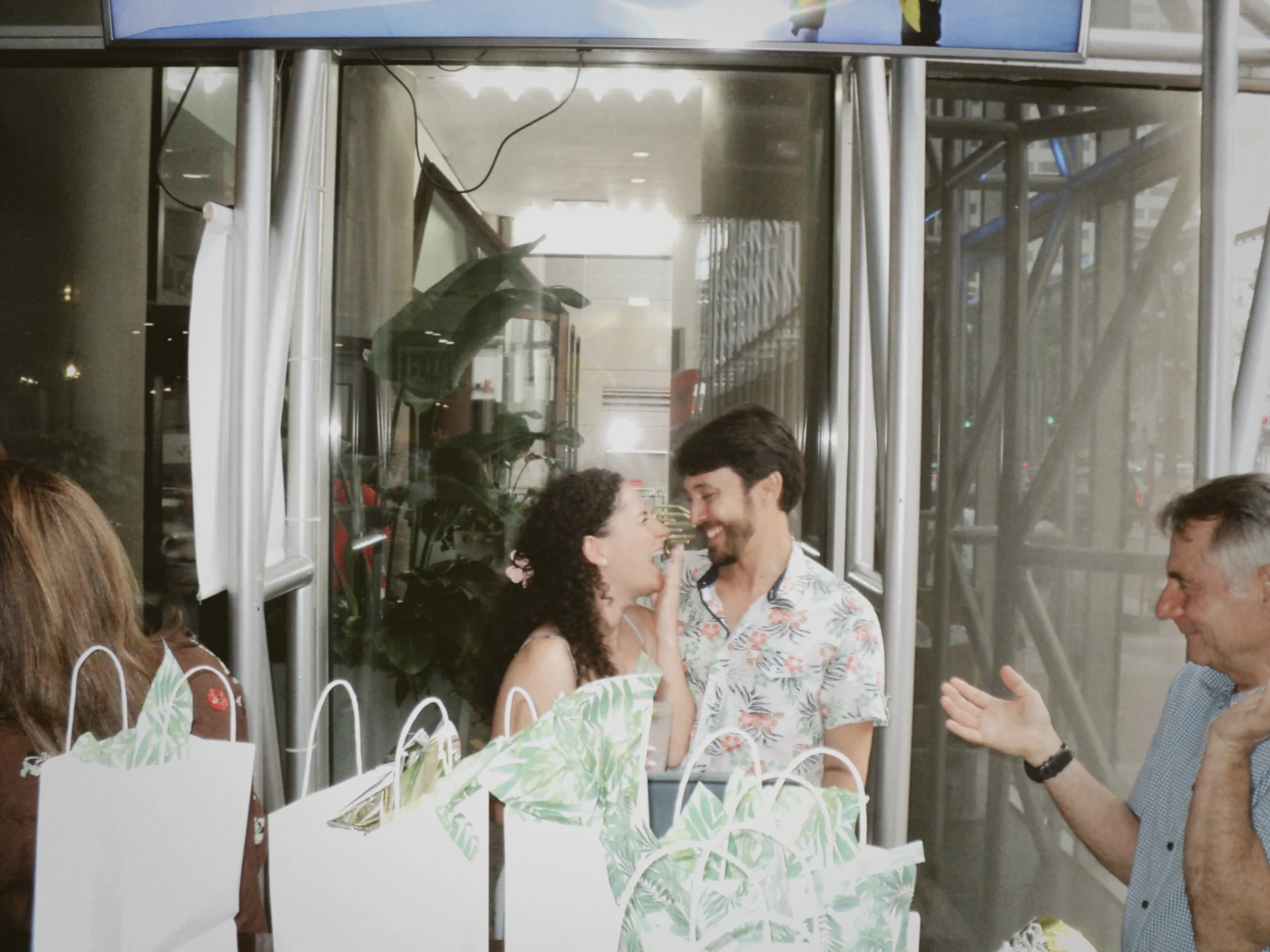 Couple sharing a candid laugh together while standing near gift bags at their wedding rehearsal dinner celebration.