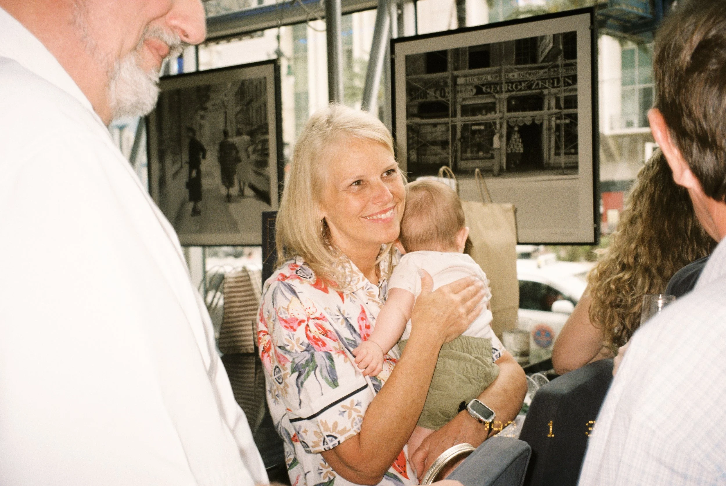 Smiling woman holding a baby while mingling with guests at the pre-wedding celebration.
