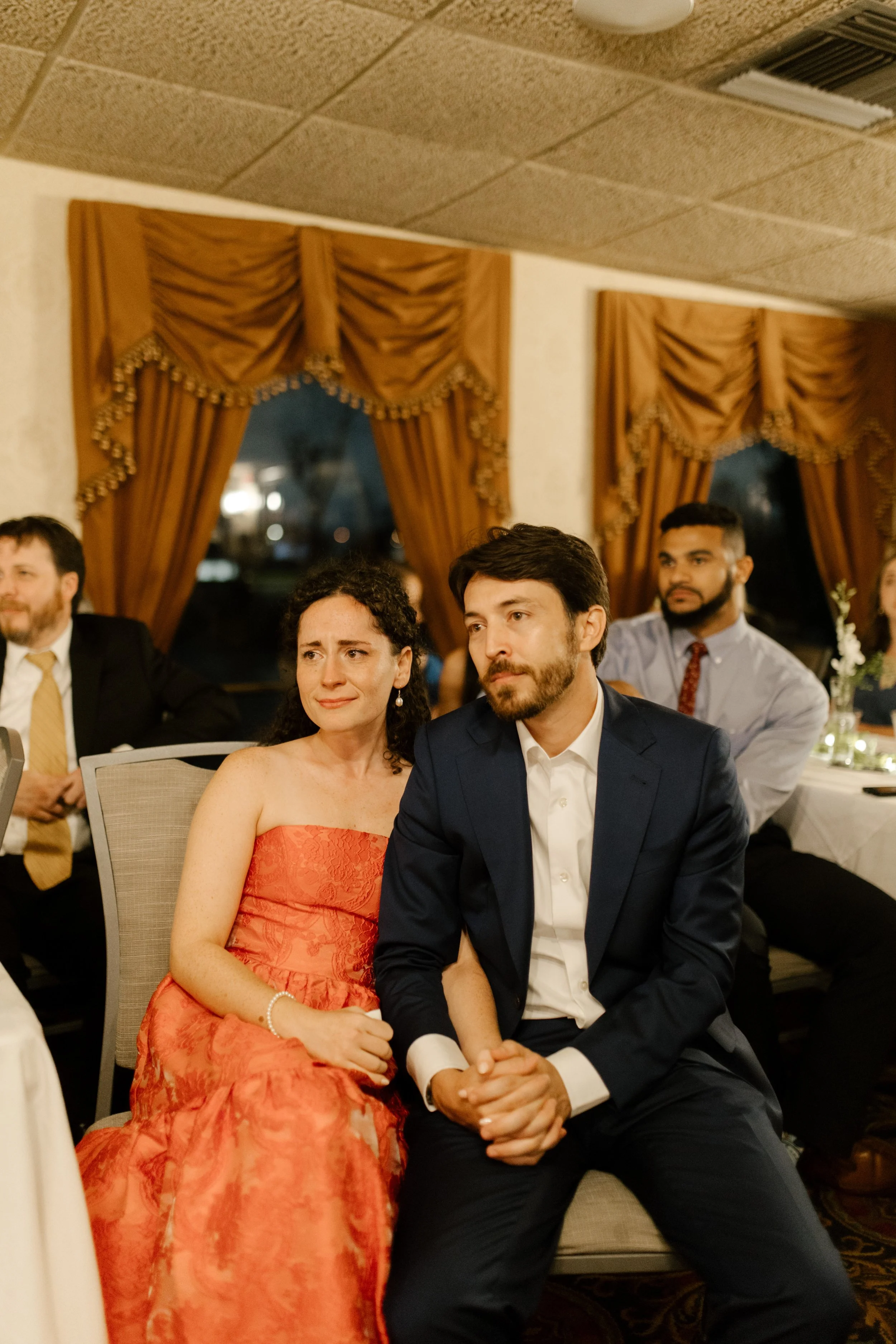 Couple sitting together and listening to a heartfelt speech during their wedding rehearsal dinner.
