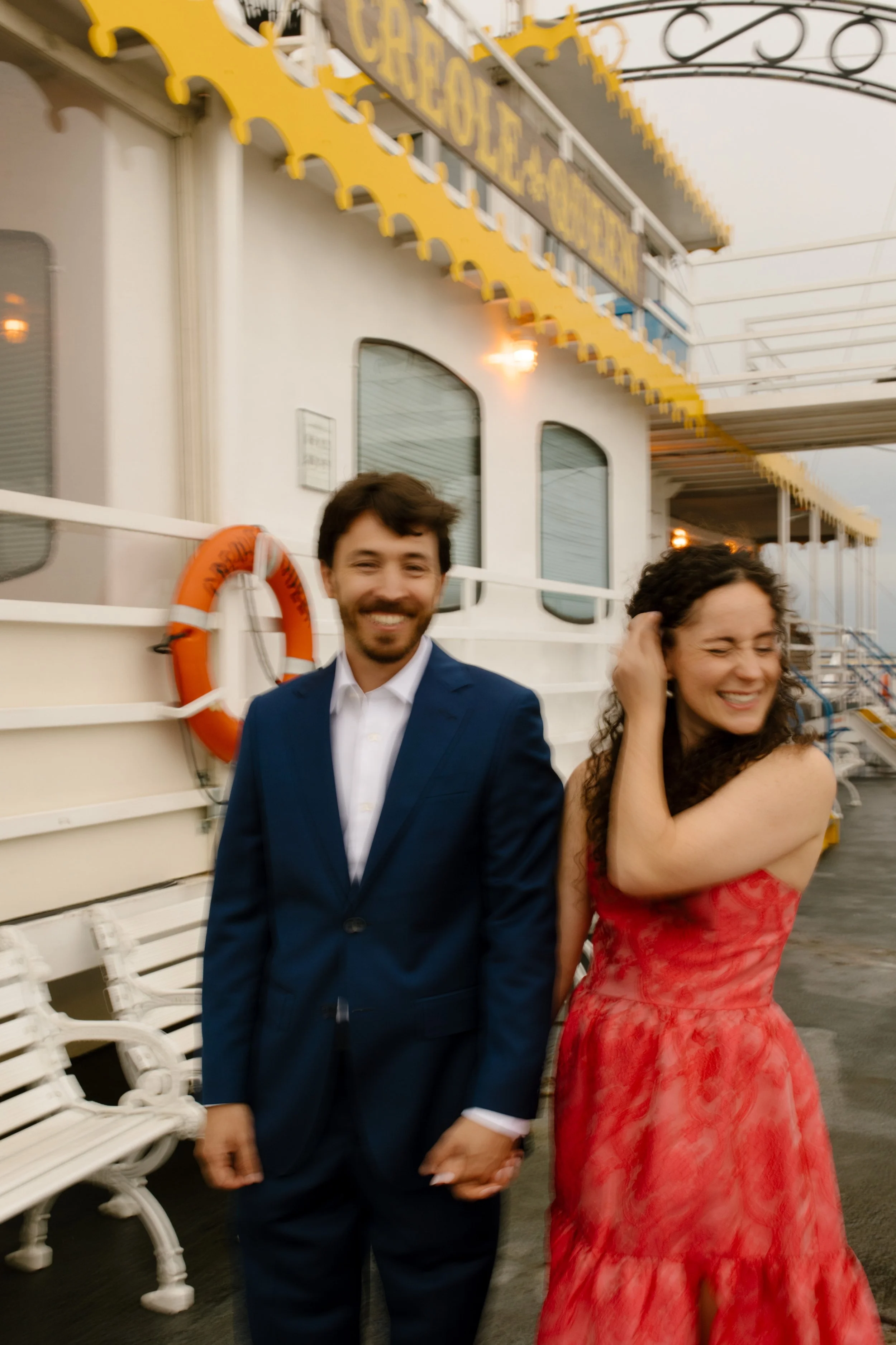 Couple holding hands and laughing together on the riverboat deck before their wedding rehearsal dinner.