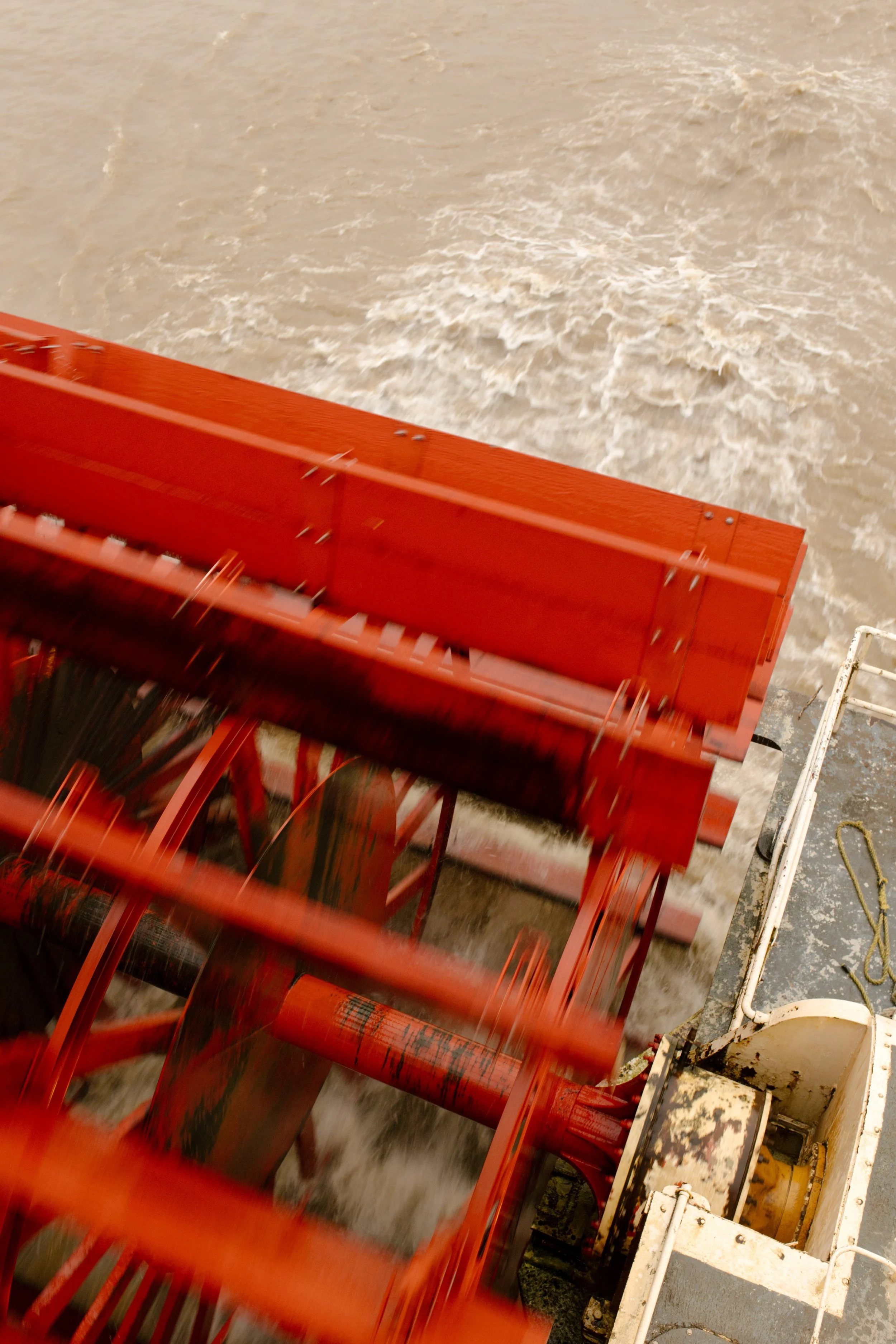 Bright red paddle wheel churning through the river behind the moving riverboat.