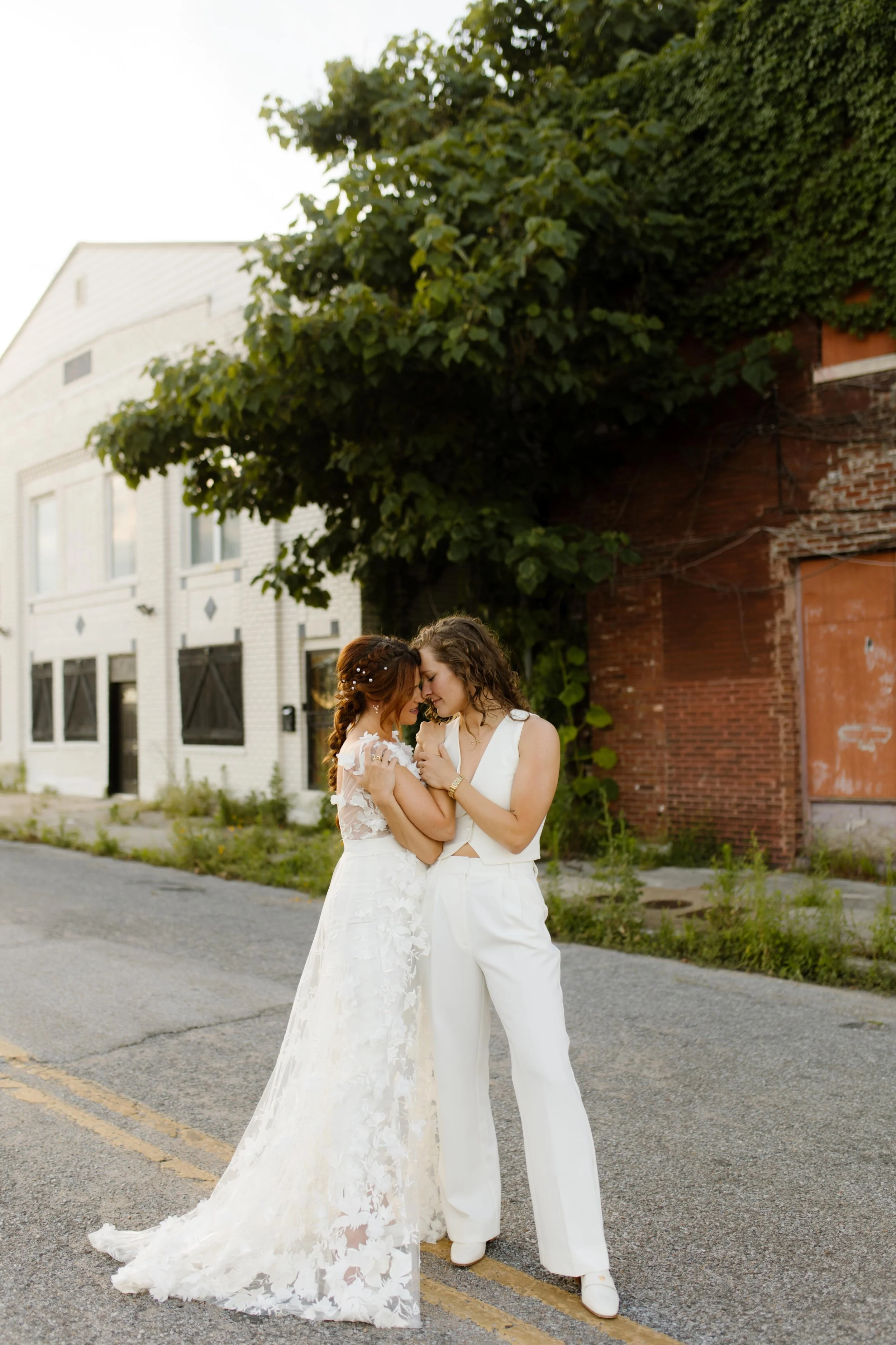 Newlyweds in a lace wedding dress and white suit sharing a romantic moment in the street