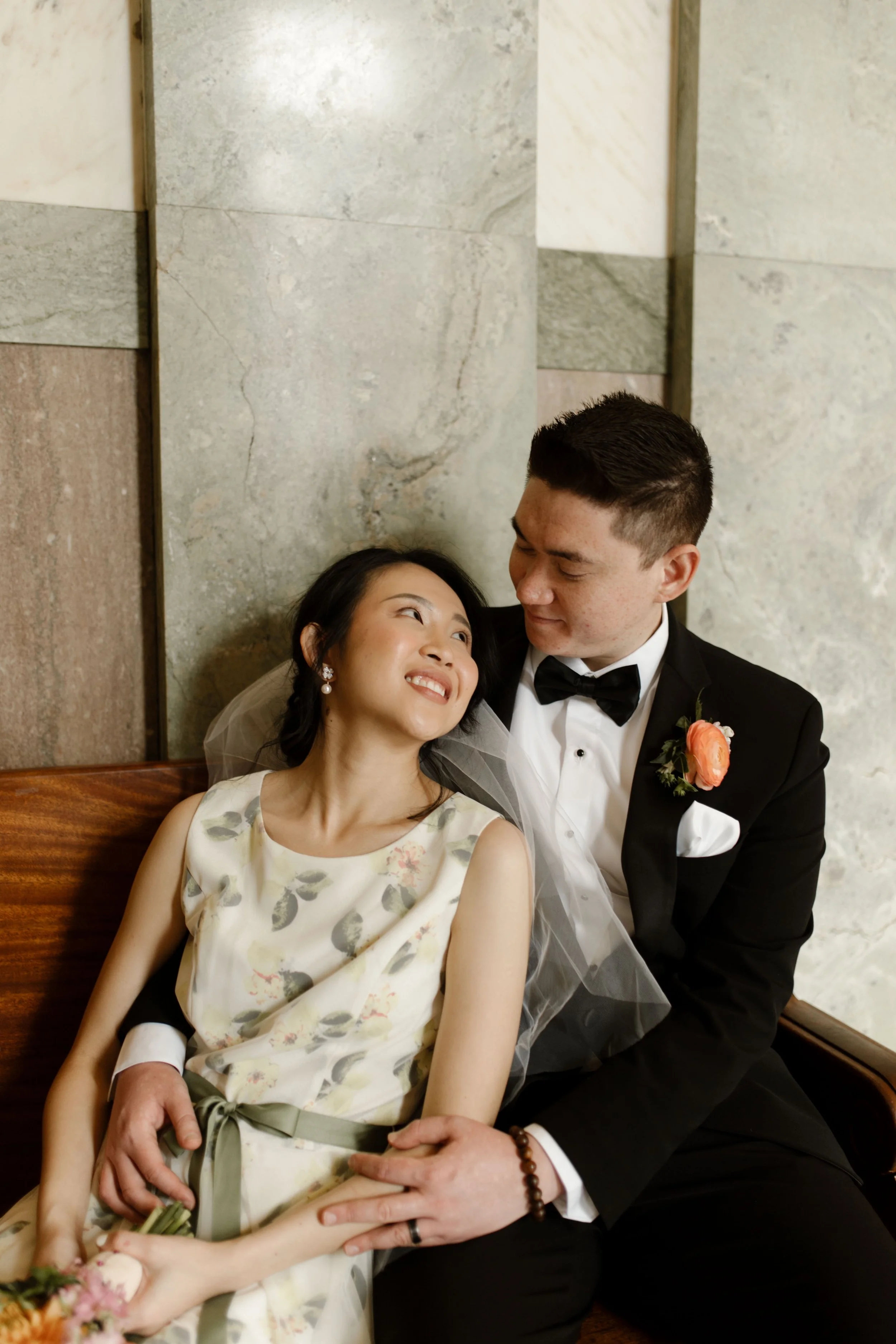 Newlyweds in a floral wedding dress and black tuxedo sitting together inside the courthouse