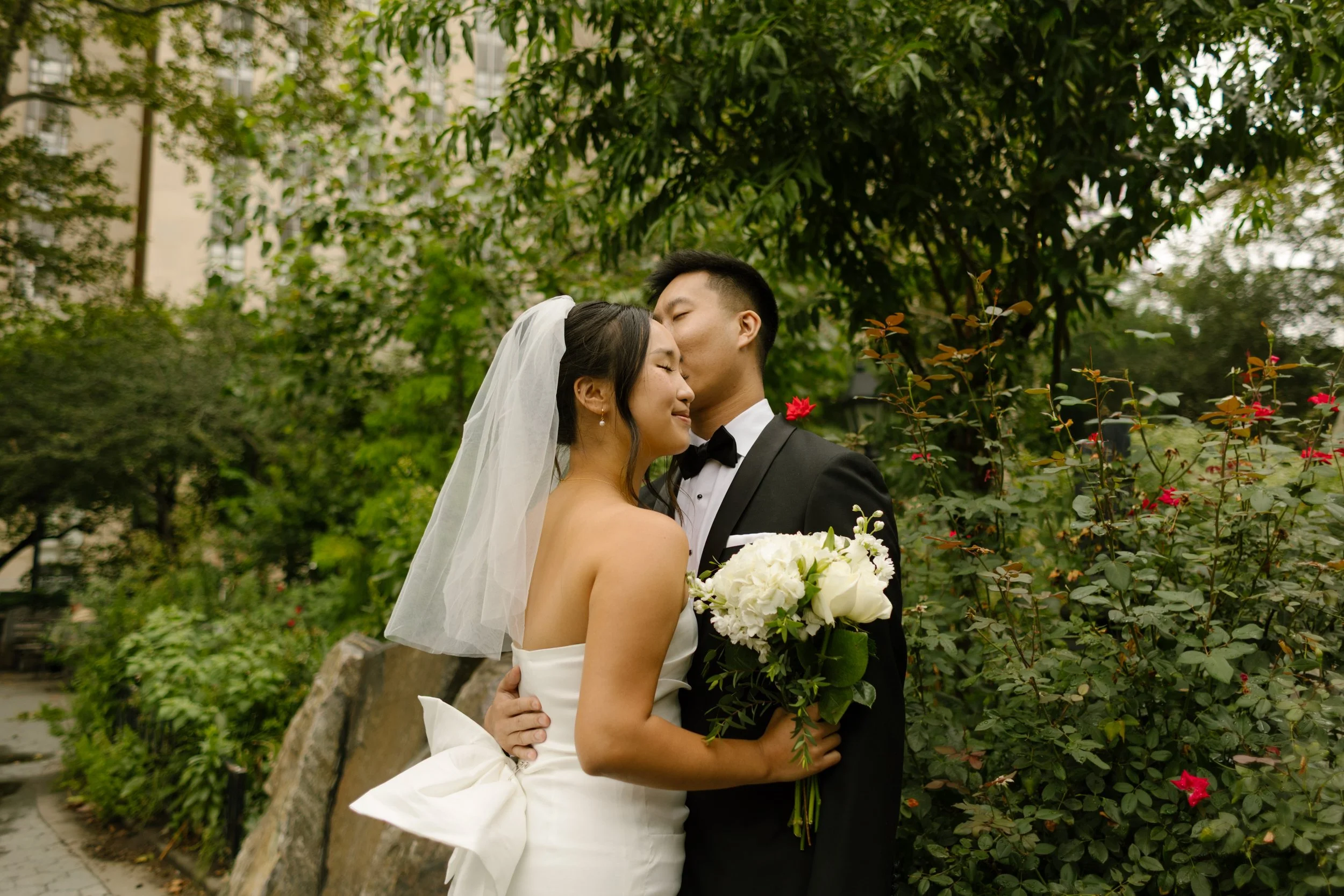 Newlyweds in a strapless white dress and black tuxedo sharing a quiet moment in a garden