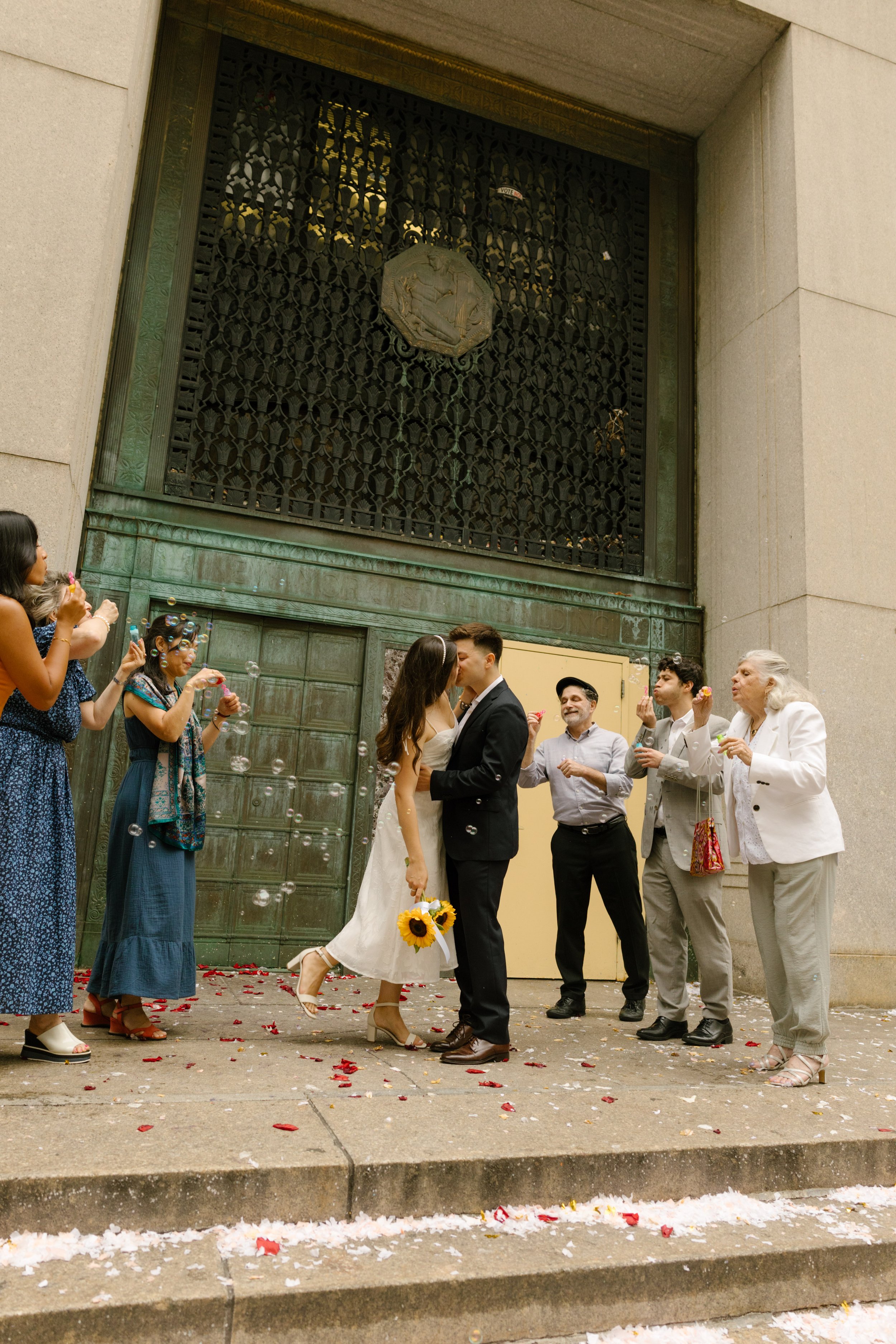 New York City courthouse wedding couple kissing outside the courthouse while family celebrates with bubbles