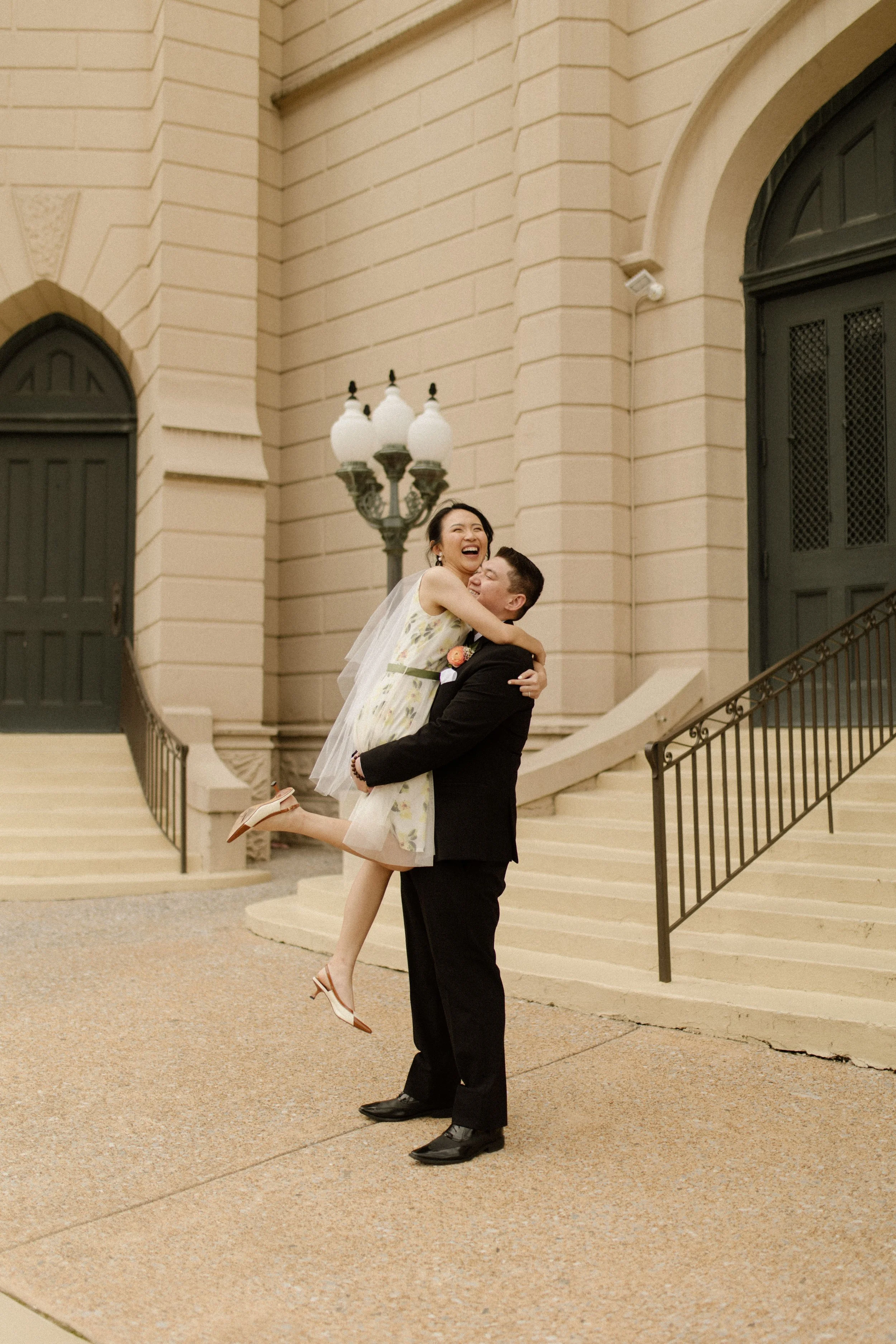 Newlyweds laughing outside the courthouse with the bride wearing a floral wedding dress and veil