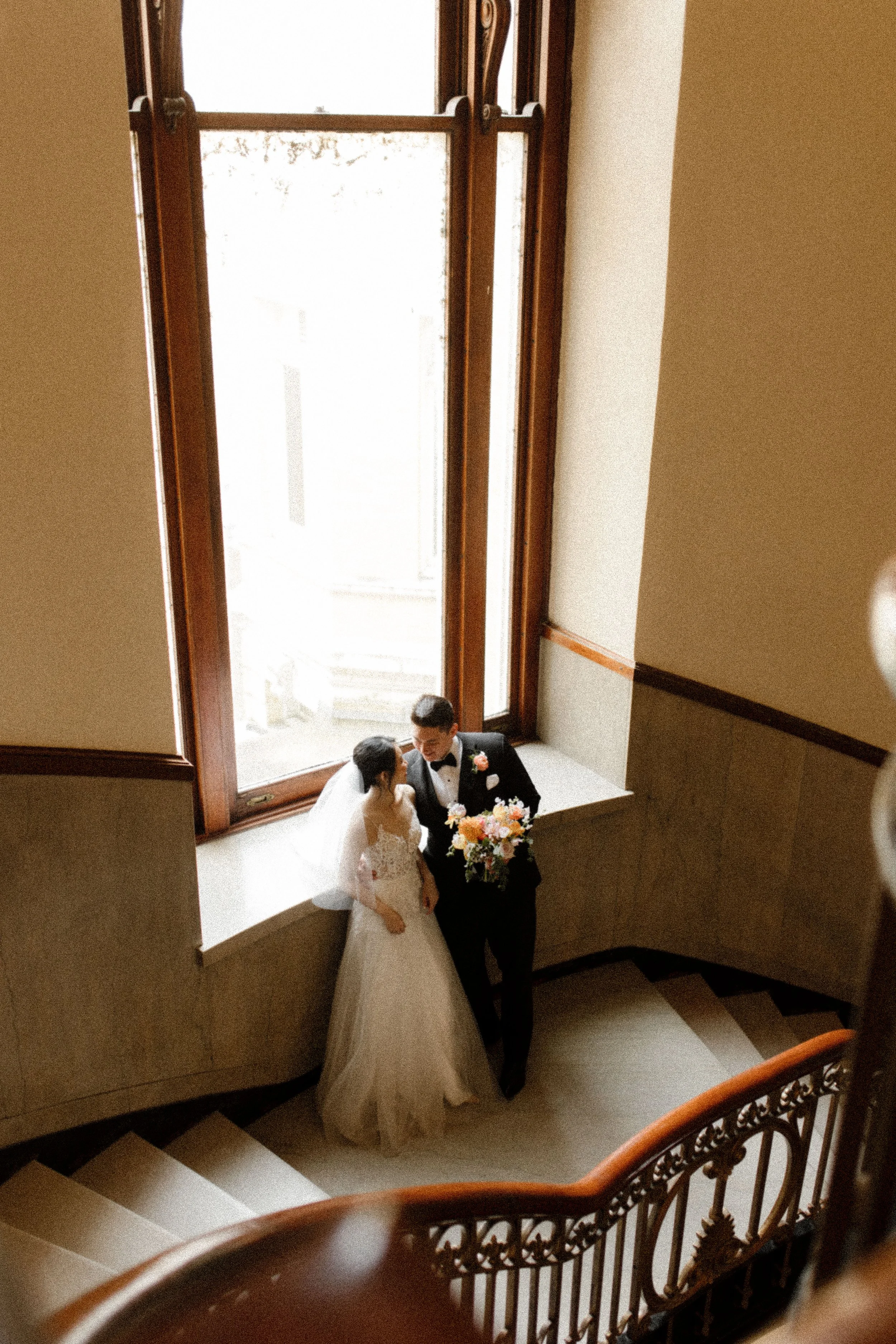 Newlyweds standing together on an ornate courthouse staircase with a colorful wedding bouquet