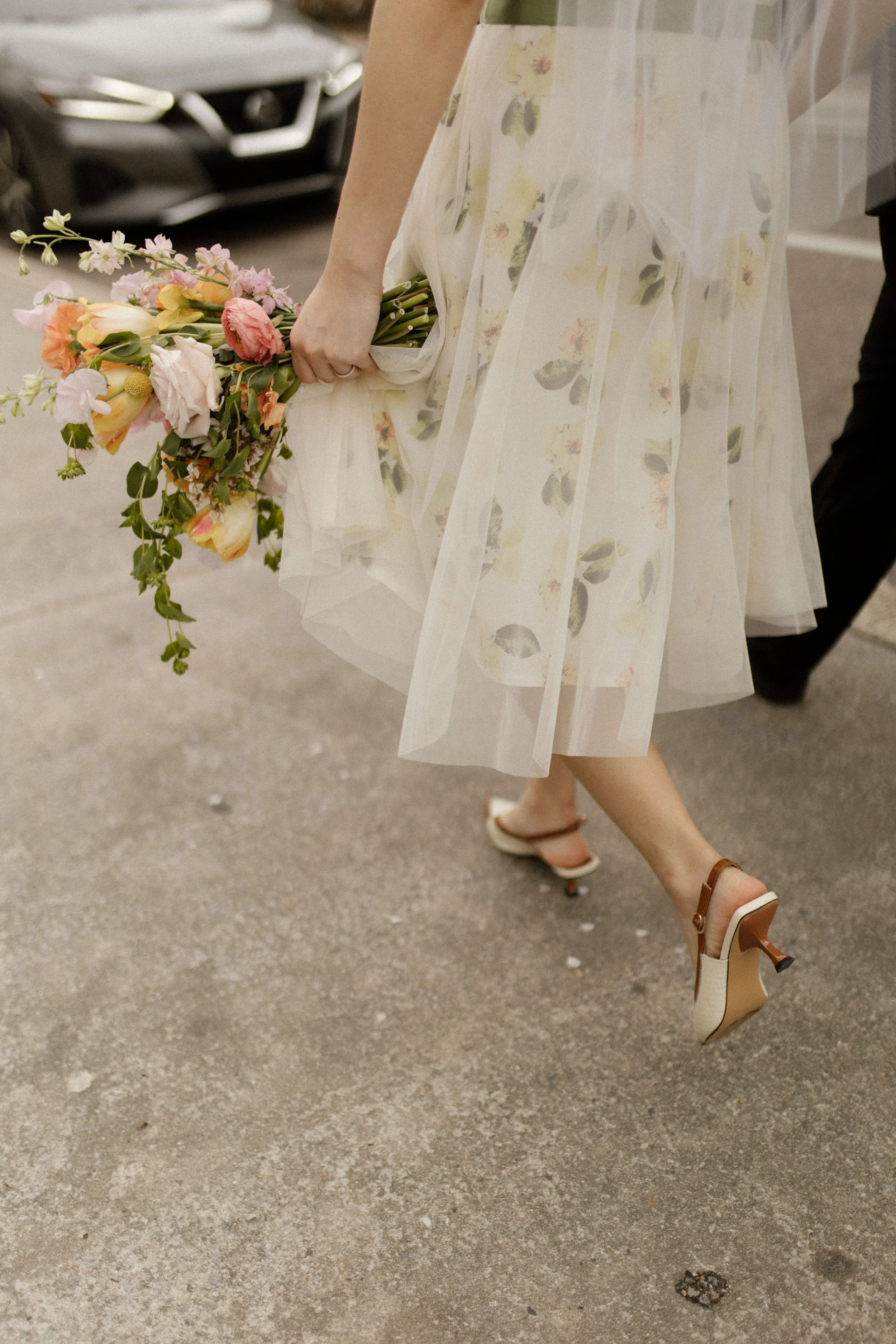 Close-up of a floral wedding dress, colorful bouquet, and vintage heels while walking after the ceremony