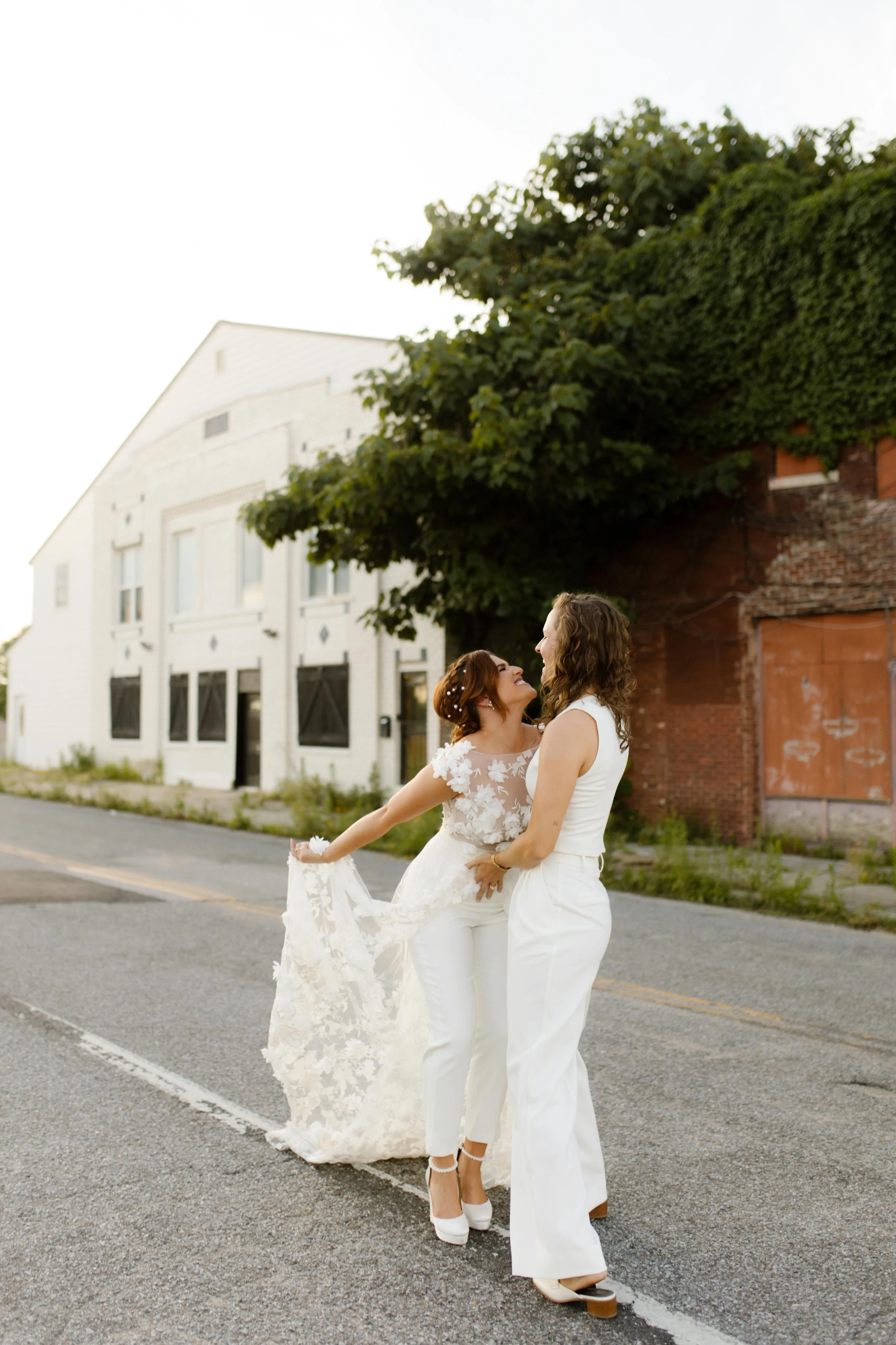 New York City courthouse wedding brides laughing together in the street while wearing modern white wedding outfits