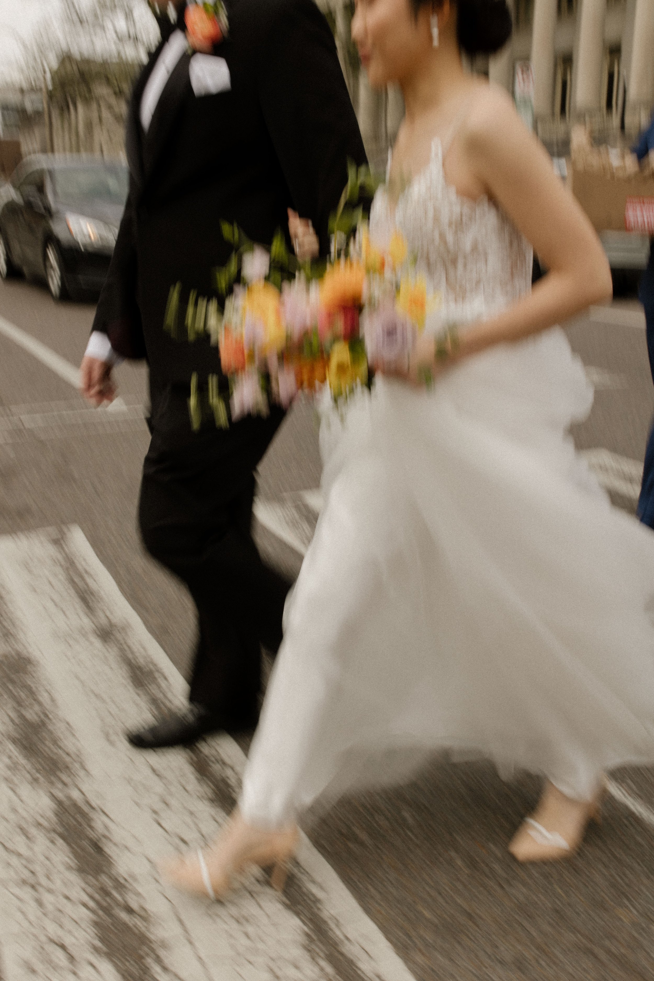 New York City courthouse wedding couple crossing the street in a lace wedding dress and black tuxedo with a colorful bouquet