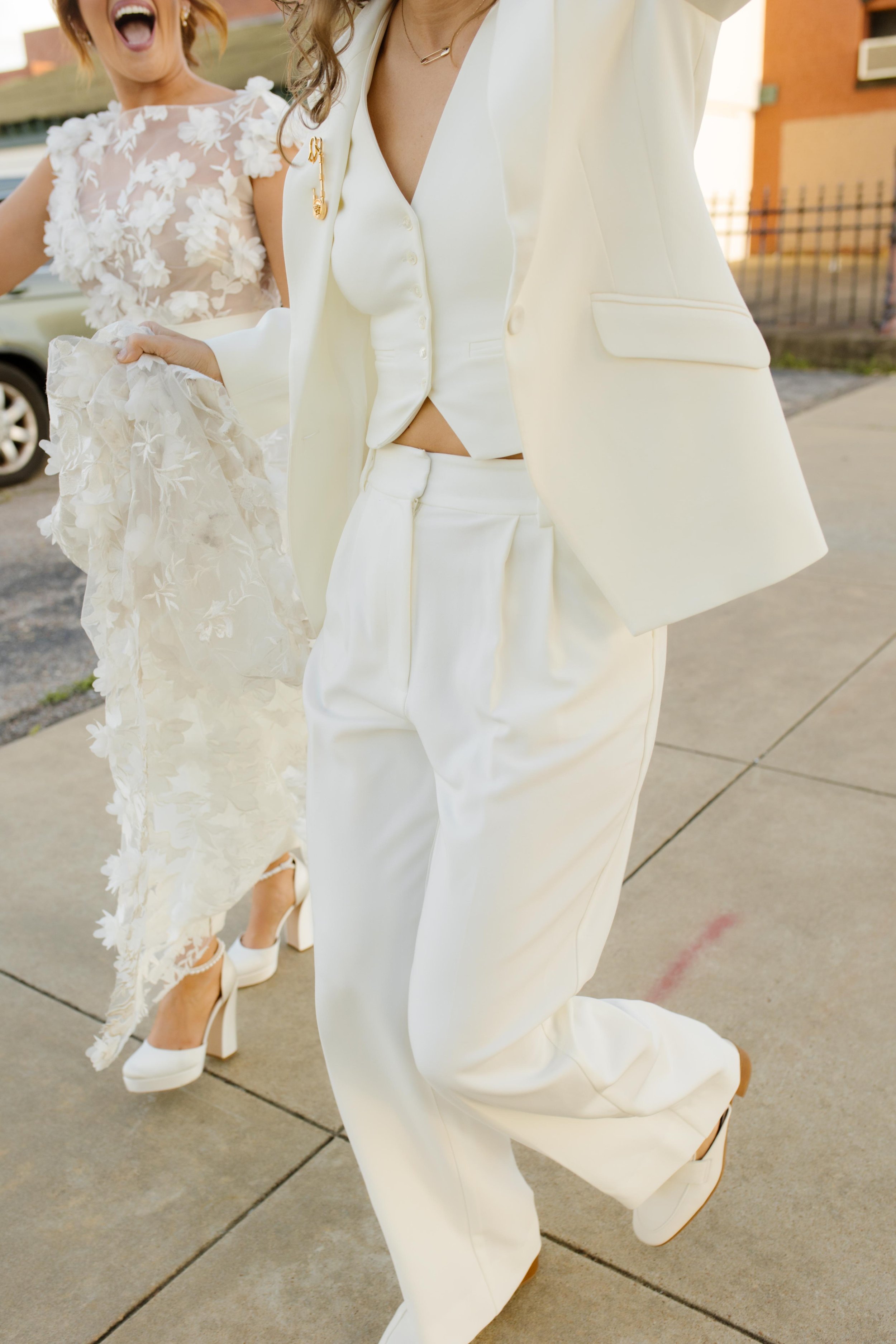 Close-up of a white wedding suit with vest and a floral lace wedding dress during a city celebration