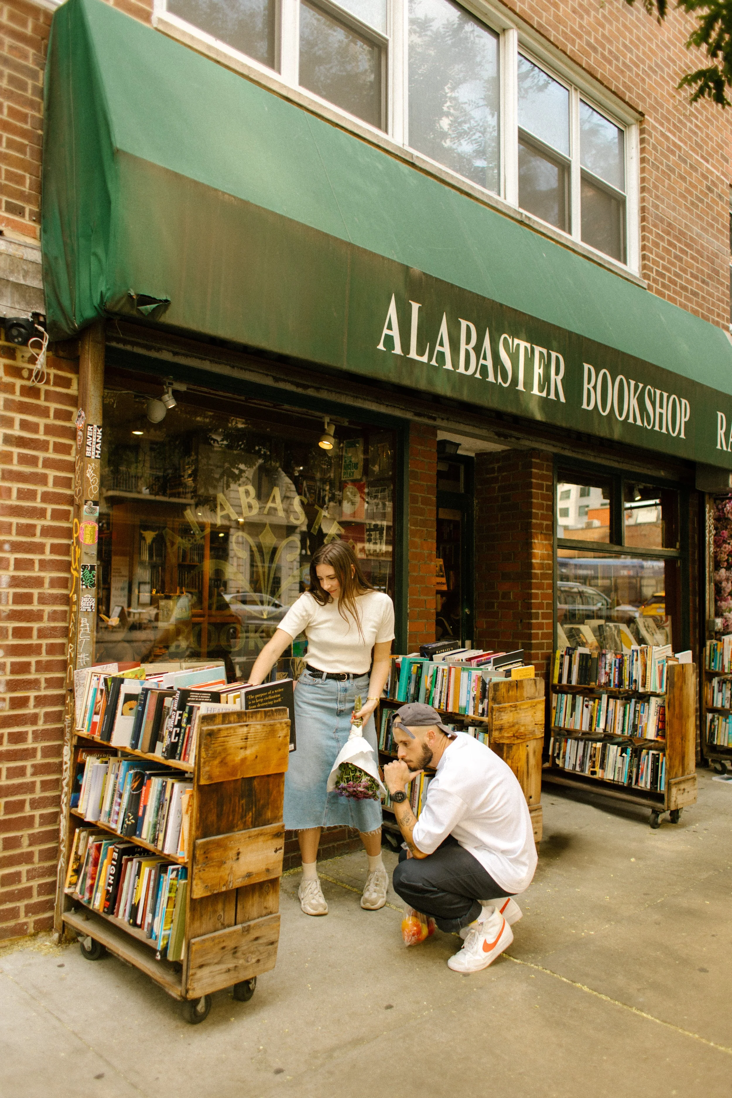 Couple browsing books outside a neighborhood bookstore during a documentary-style engagement session in New York City.