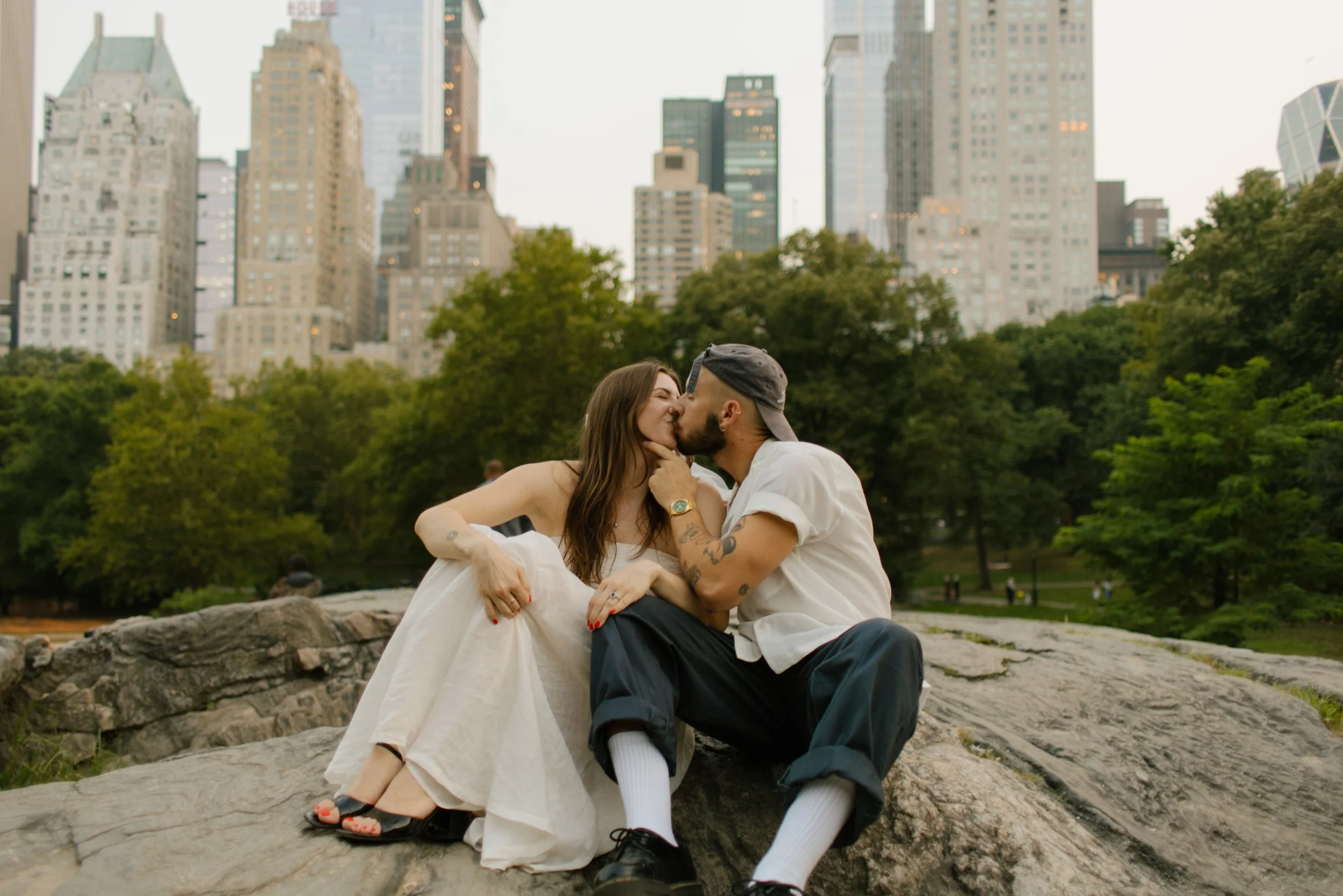 Bride and groom sharing a kiss in Central Park with the Manhattan skyline in the background at golden hour.