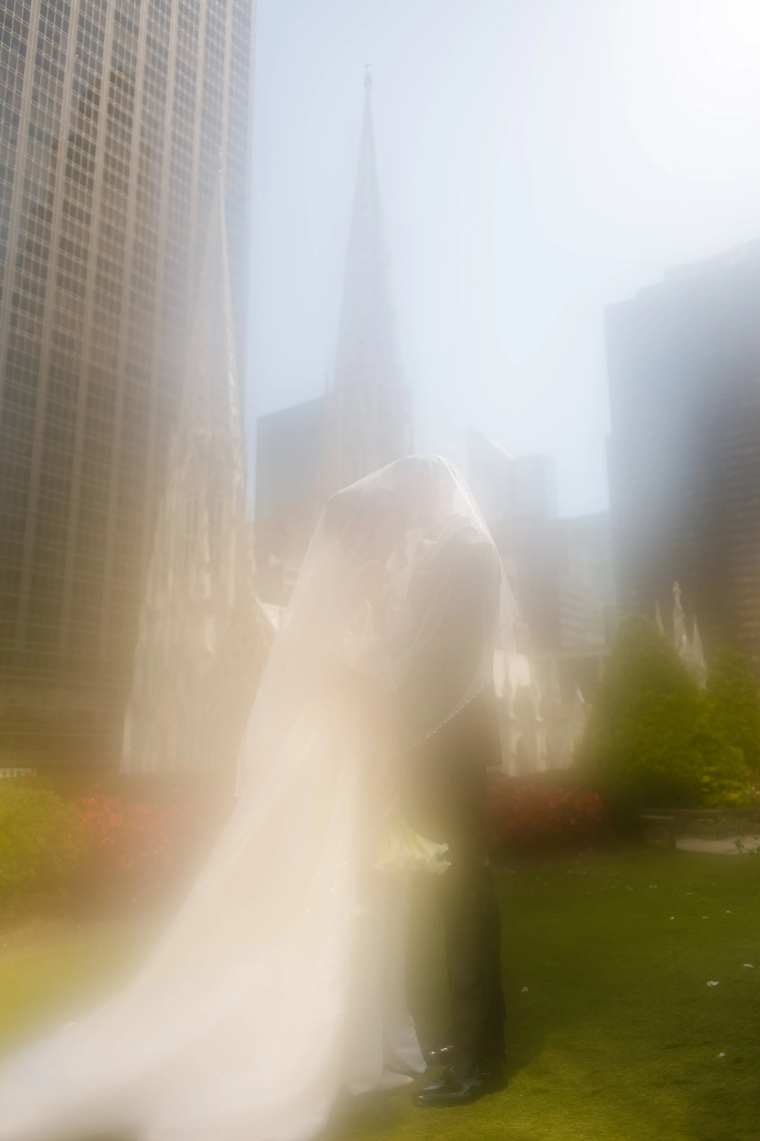 Dreamy soft-focus portrait of a bride and groom embracing amid towering New York City buildings.