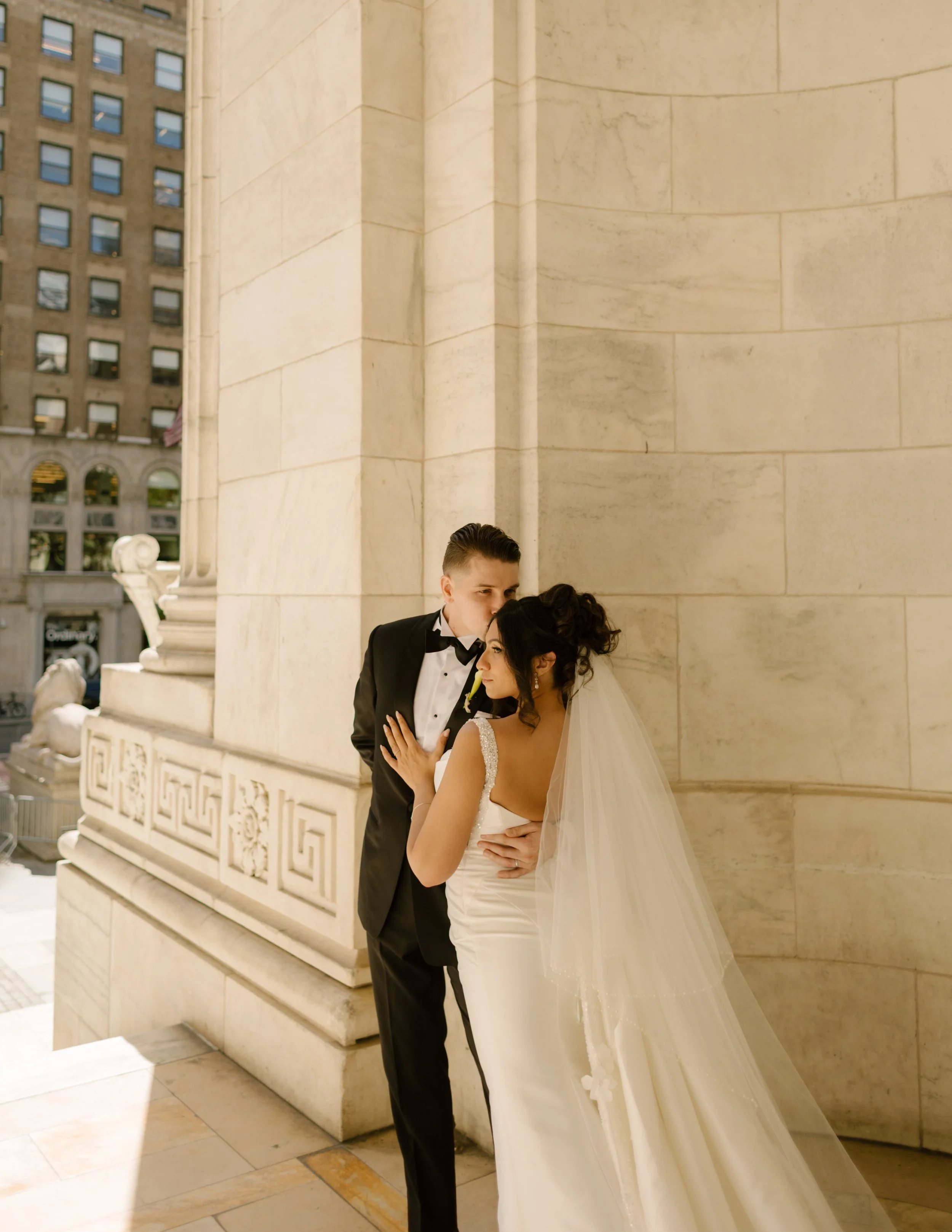 Bride and groom embrace beside an elegant stone column at one of the timeless wedding locations in New York.