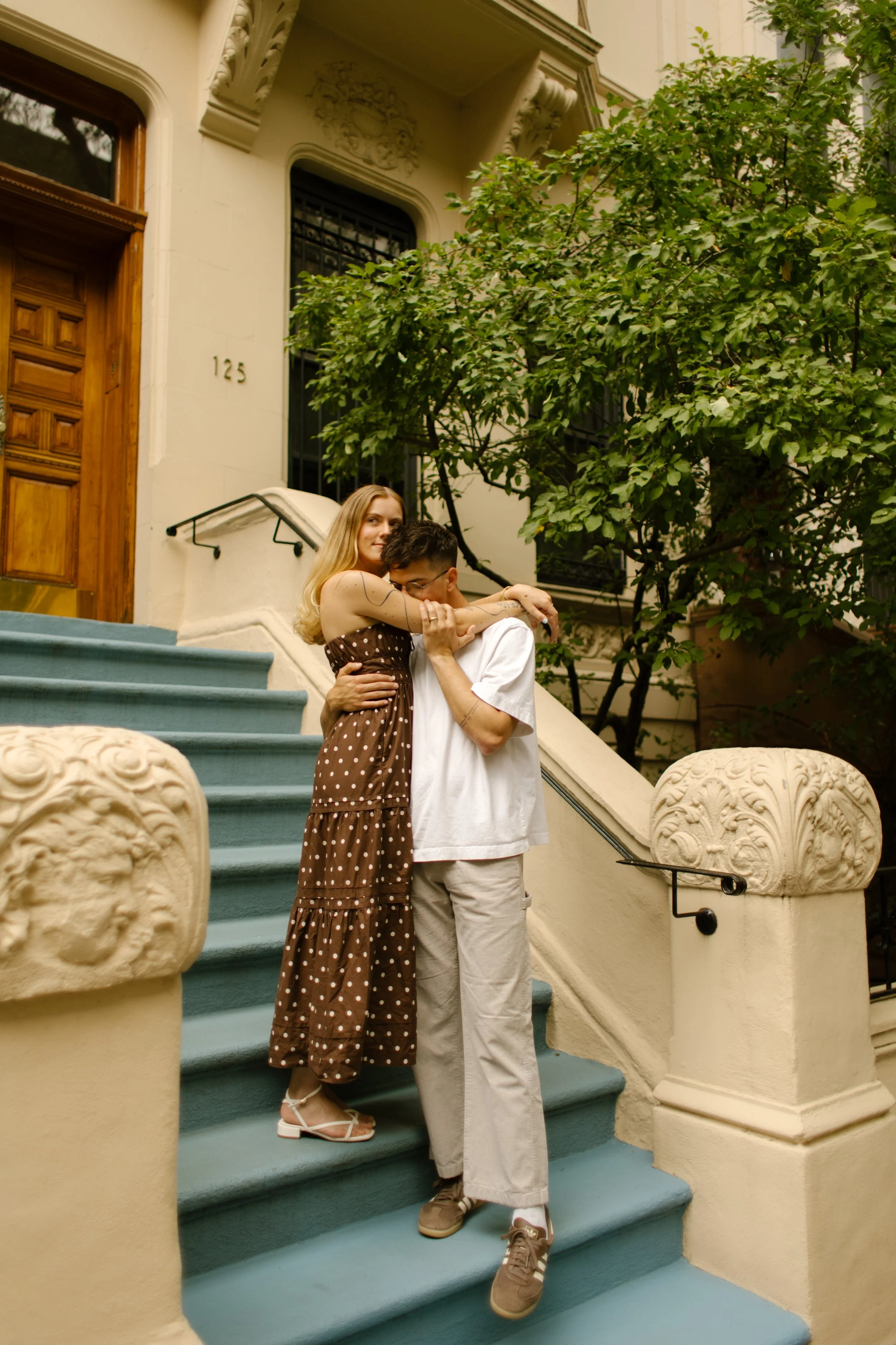 Couple share a playful embrace on the steps of a colorful New York City brownstone.