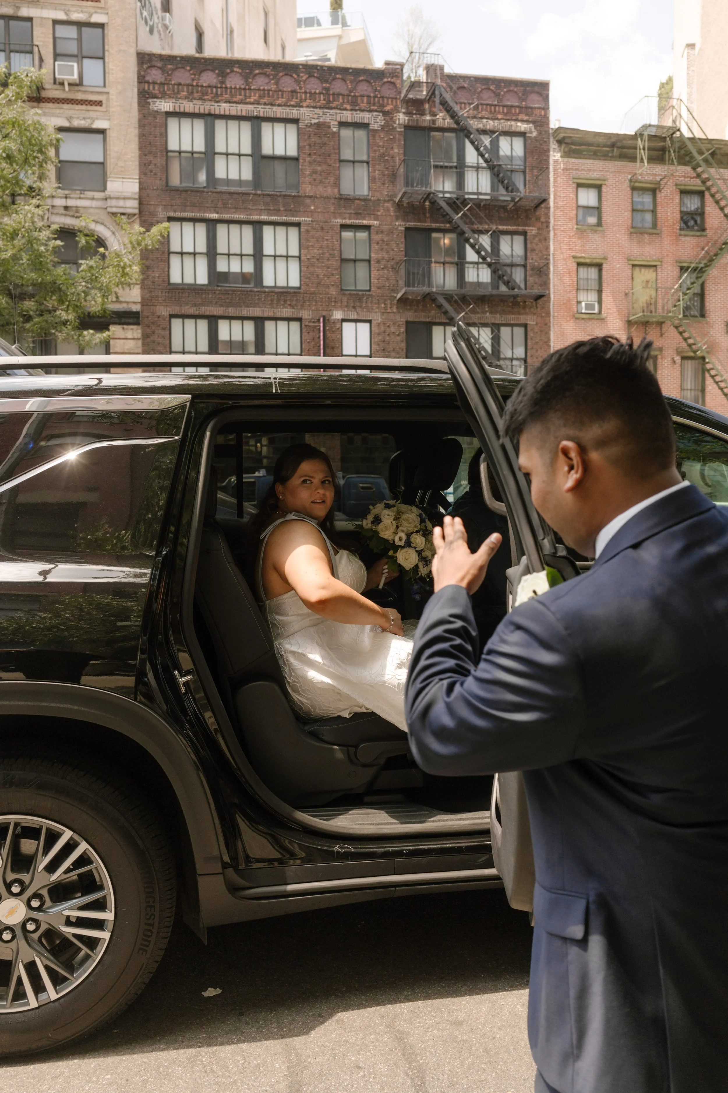 Bride steps from a car holding her bouquet as the groom greets her outside one of the intimate wedding locations in New York.