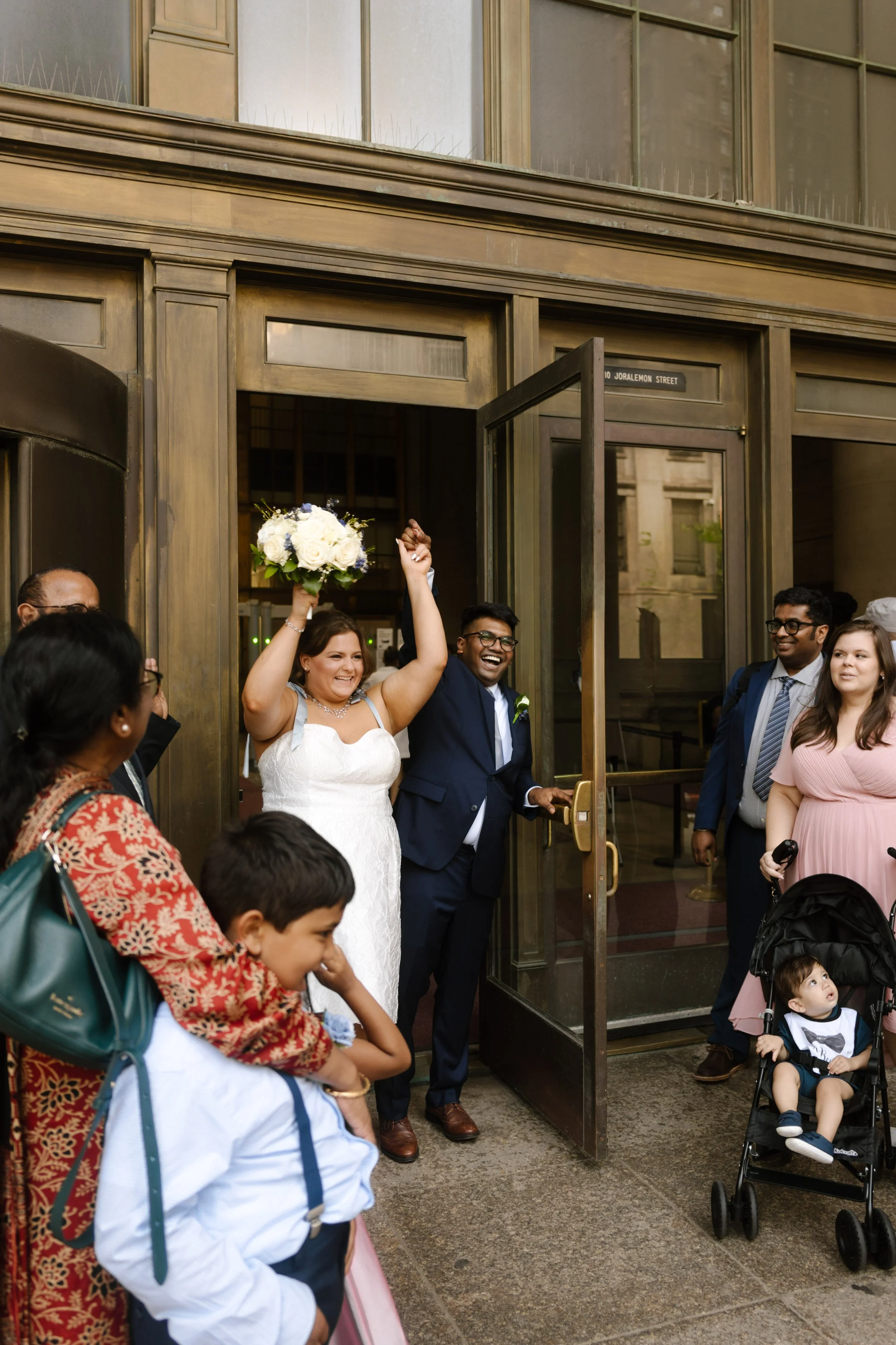 Newlyweds celebrate outside a city building surrounded by family and friends at one of the lively wedding locations in New York.