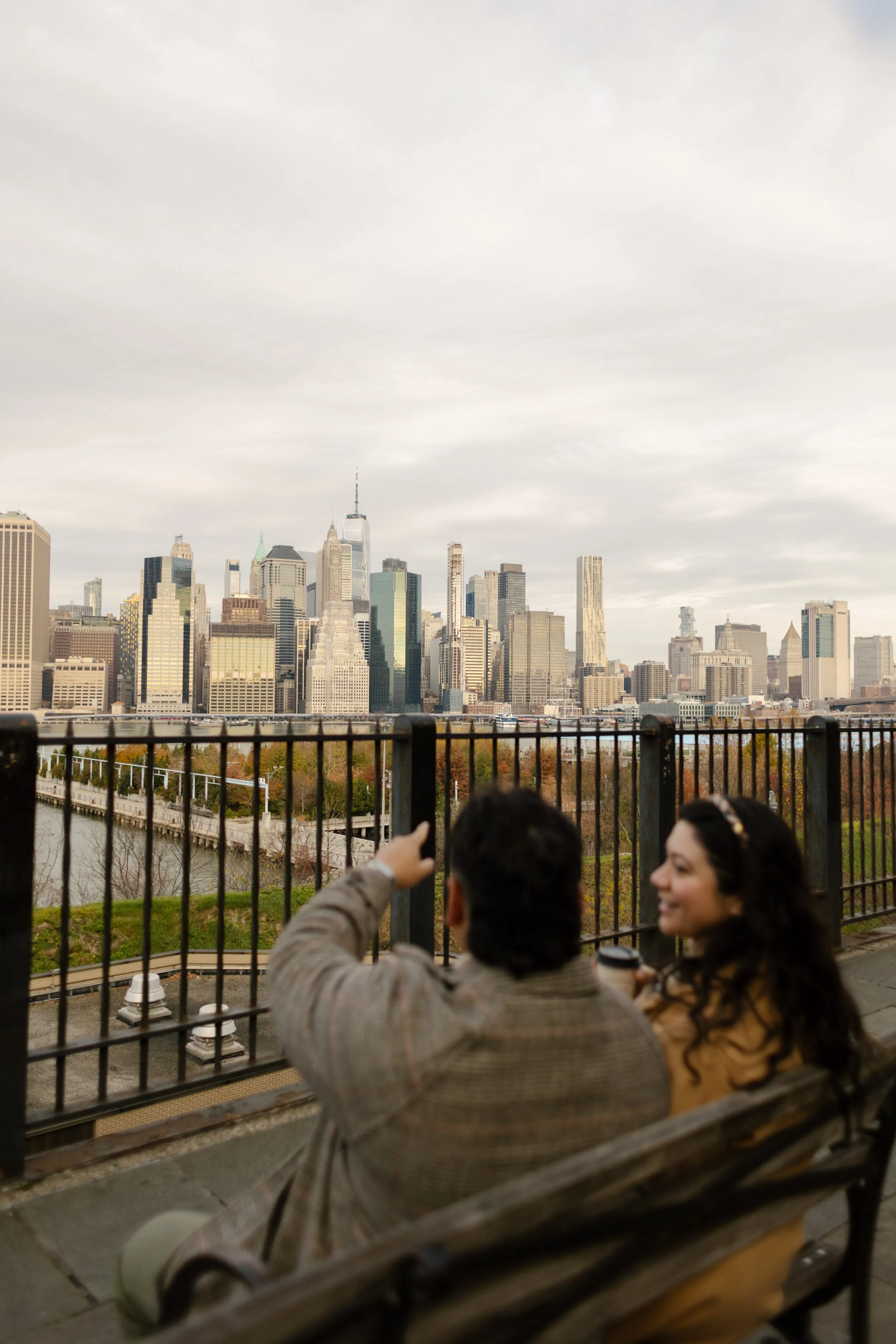 Couple relax on a waterfront bench overlooking the Manhattan skyline across the river.