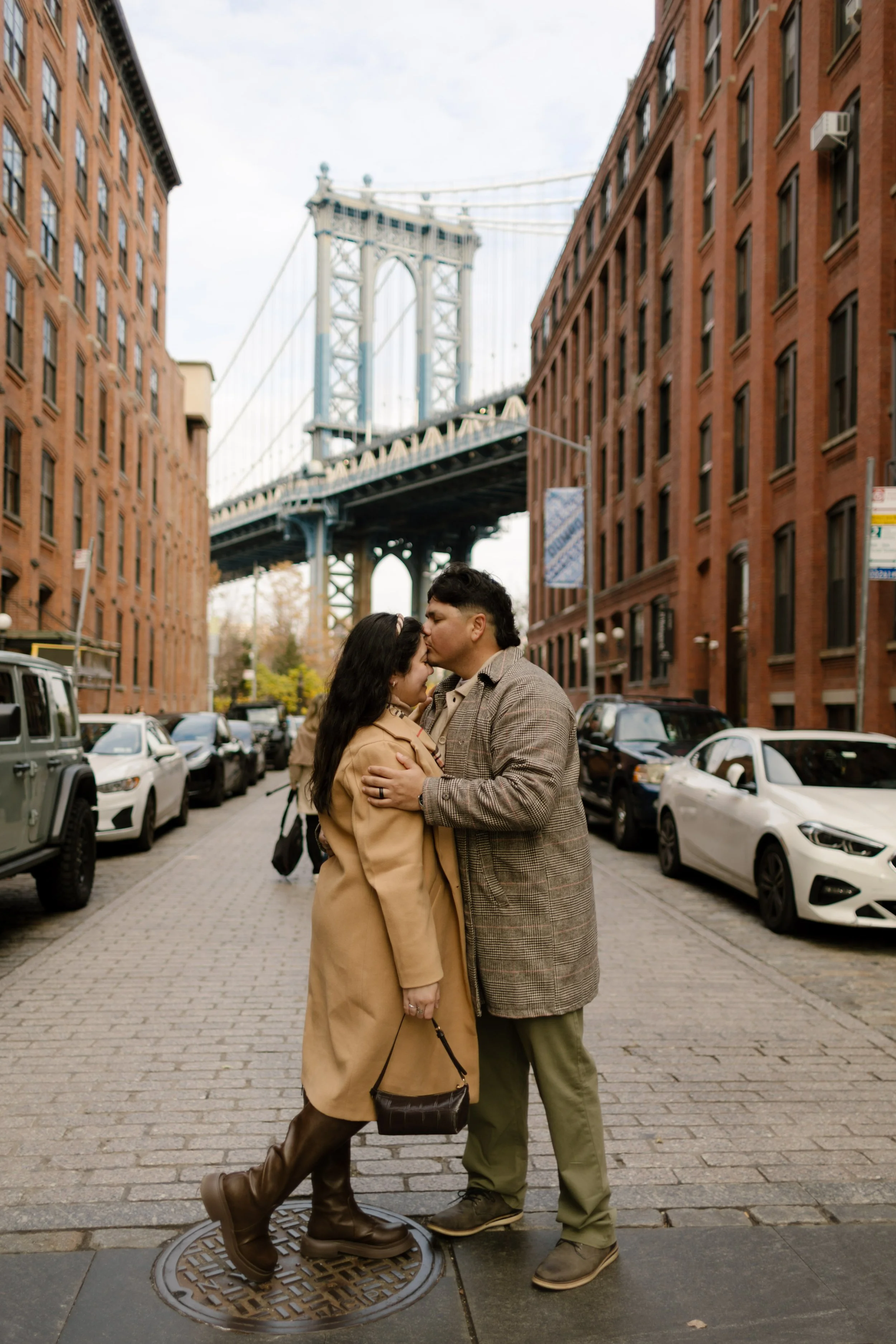 Couple kiss on a cobblestone street with the Manhattan Bridge behind them, highlighting iconic wedding locations in New York.
