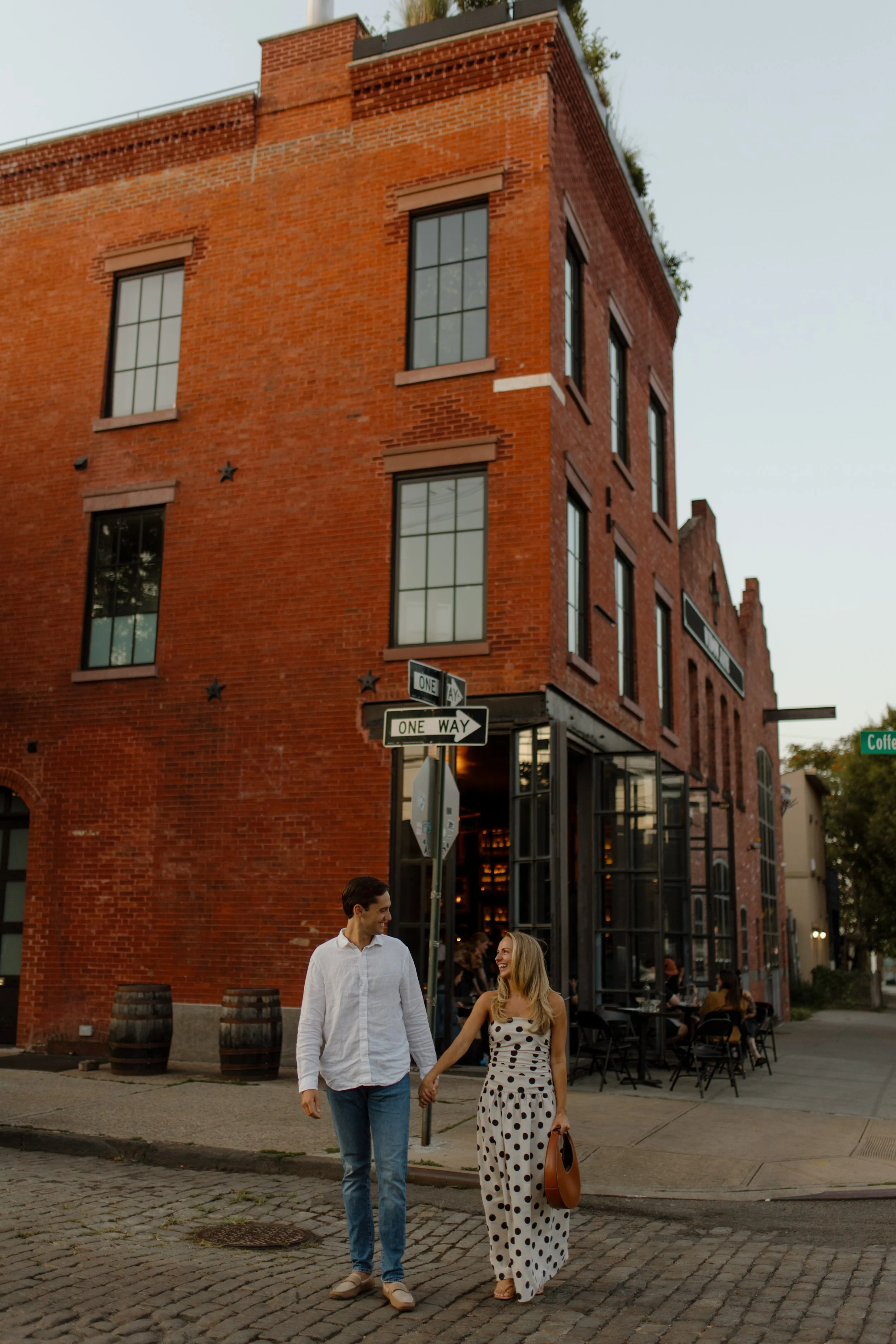 Couple walk together along a cobblestone street beside a historic red-brick building at one of the charming wedding locations in New York.