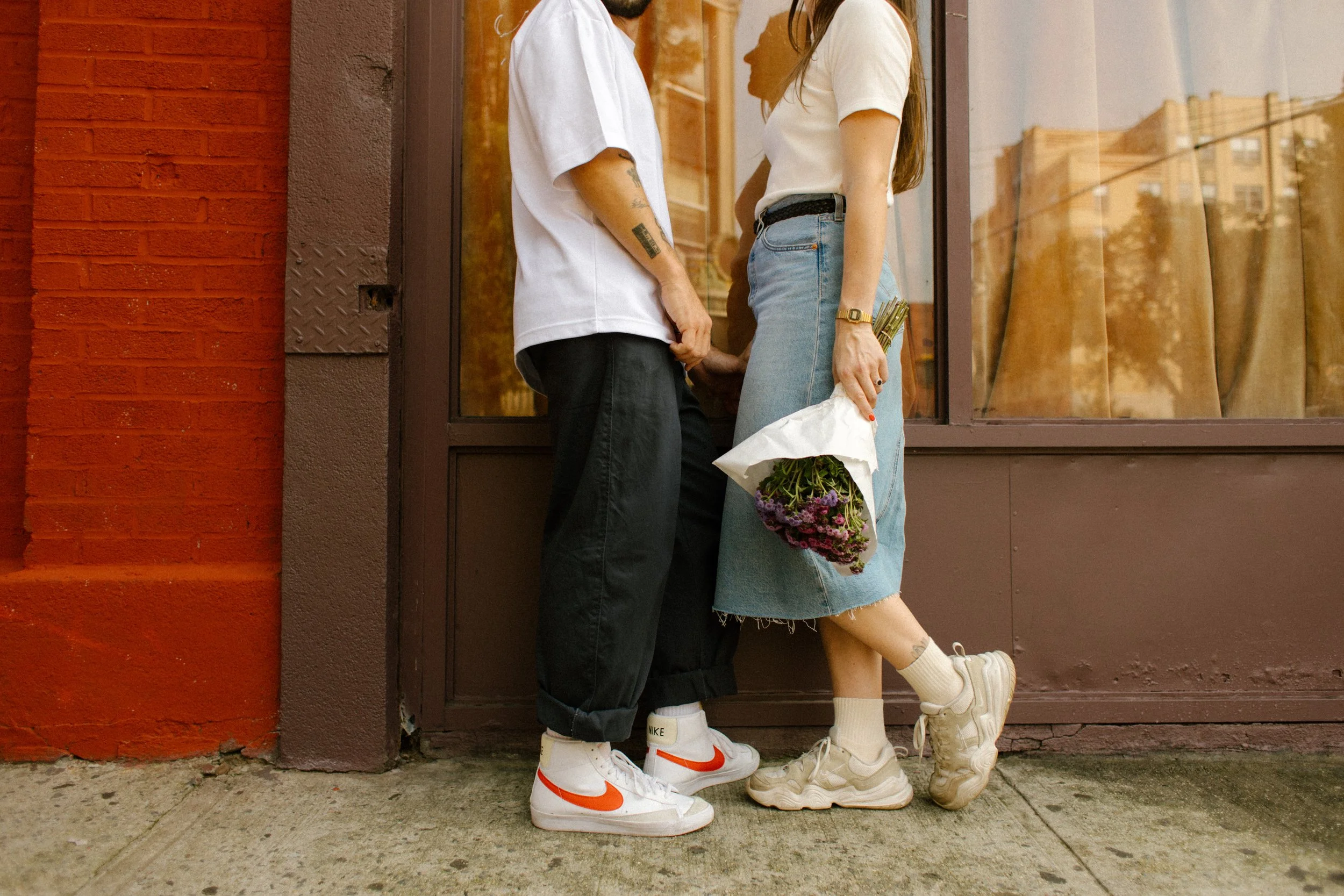 Couple share a playful moment outside a neighborhood storefront during a casual session at one of the unique wedding locations in New York.