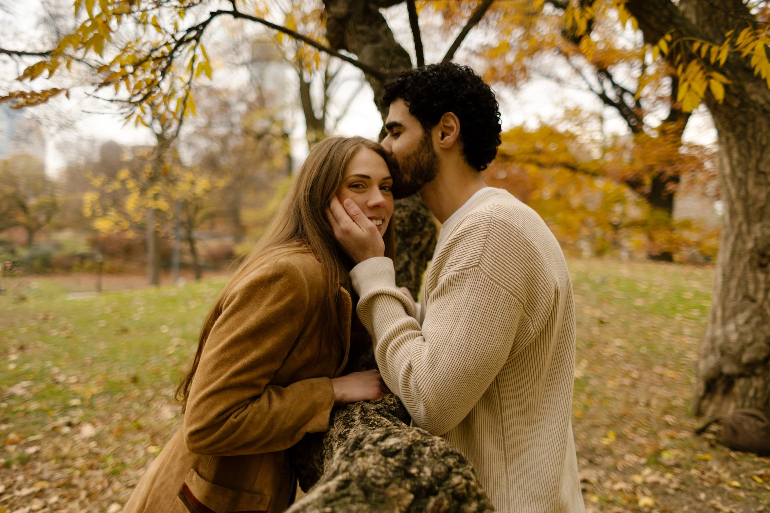 Couple share an affectionate moment surrounded by colorful autumn foliage in a New York City park.