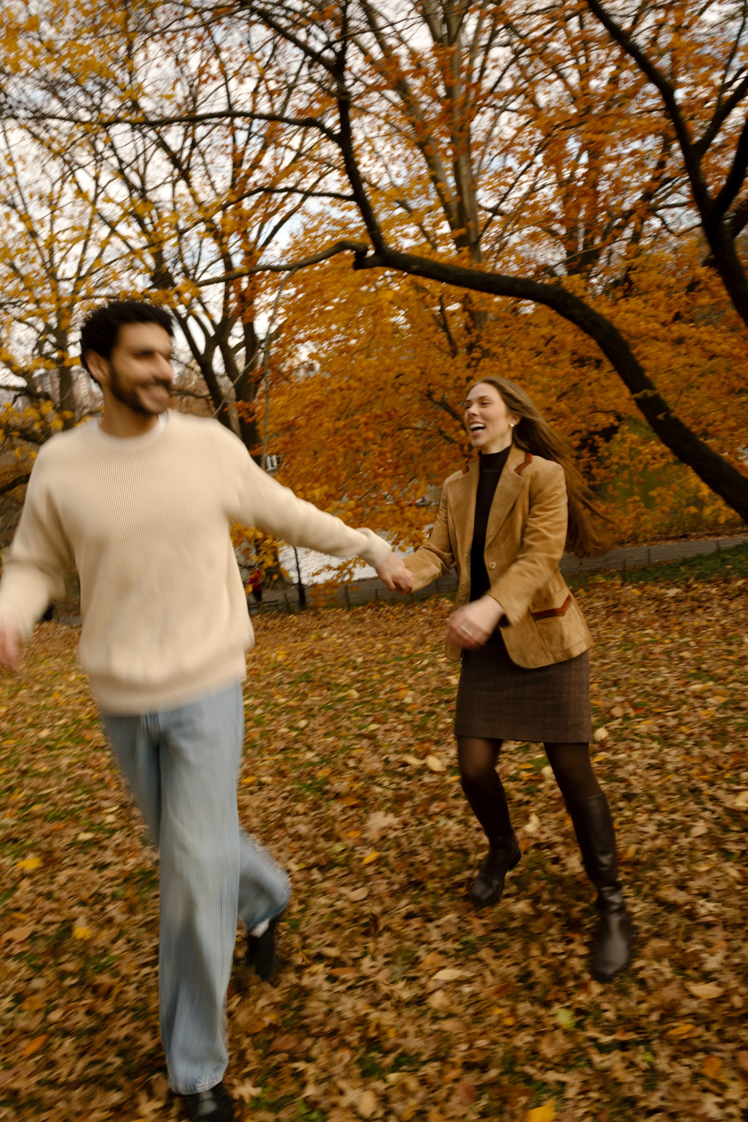 Laughing couple run hand in hand beneath vibrant fall trees at one of the scenic wedding locations in New York.