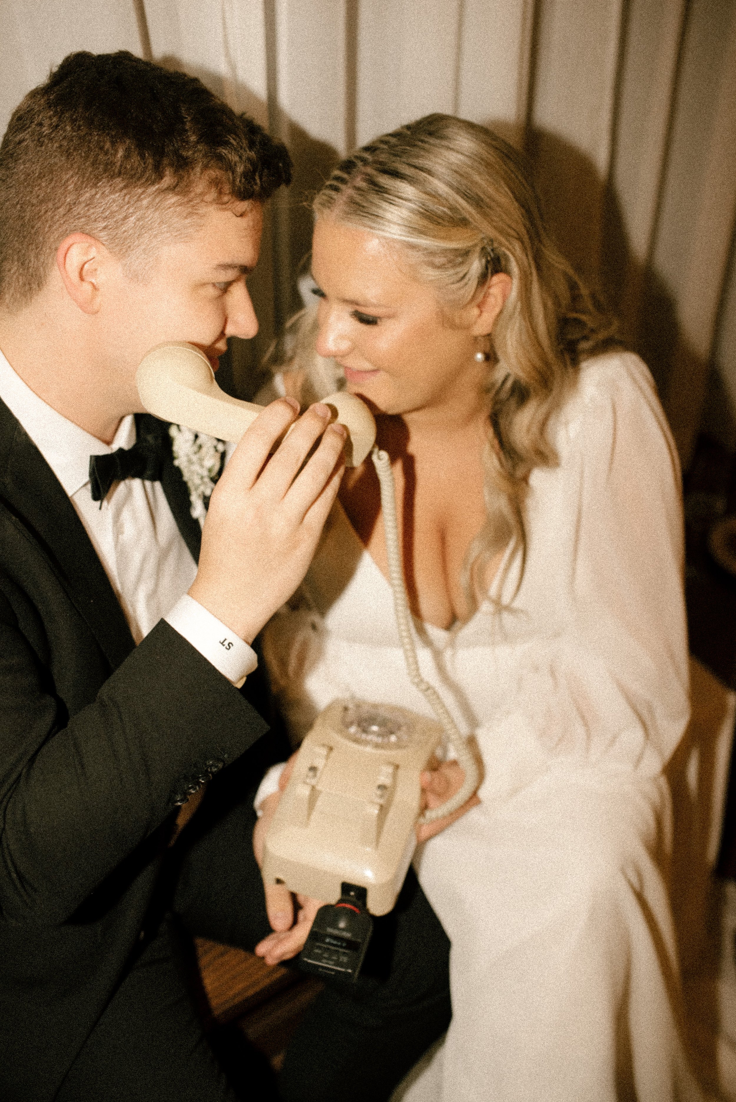 Candid reception photo of the bride and groom laughing together while using a vintage telephone audio guest book.