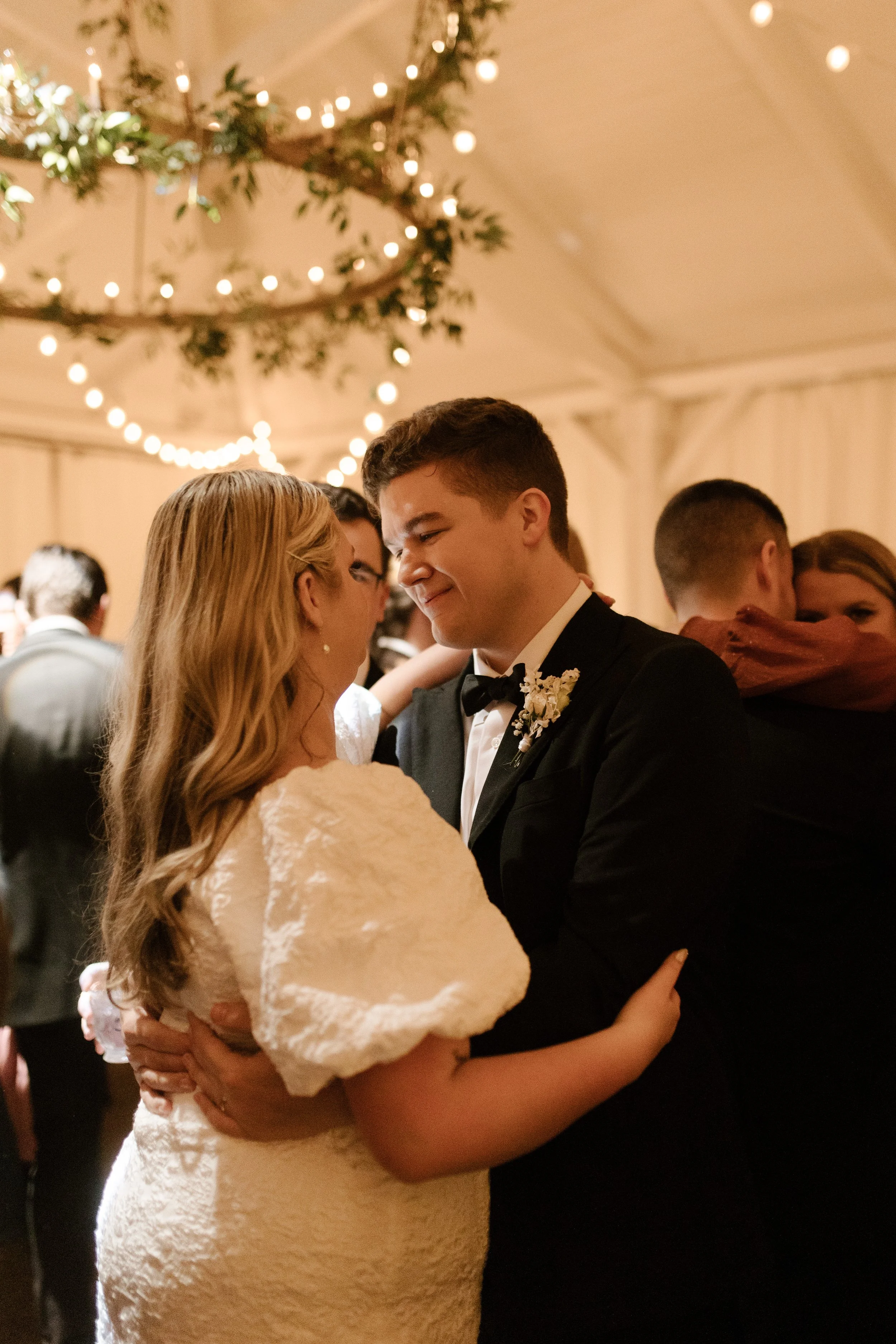 Bride and groom embracing on the dance floor beneath string lights during their fall wedding reception.