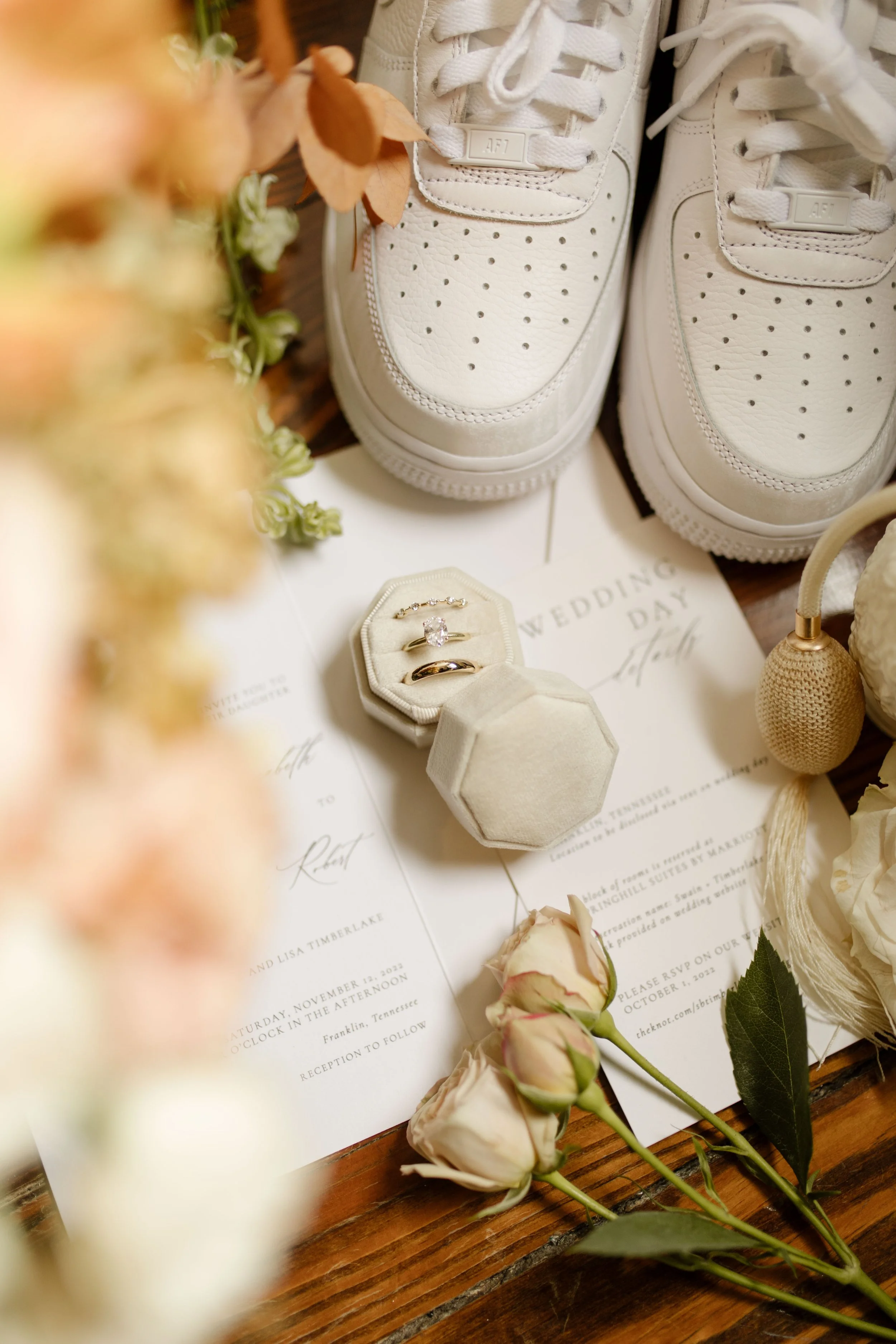 Wedding detail flat lay with white sneakers, invitation suite, wedding rings, blush roses, and vintage-inspired accessories.