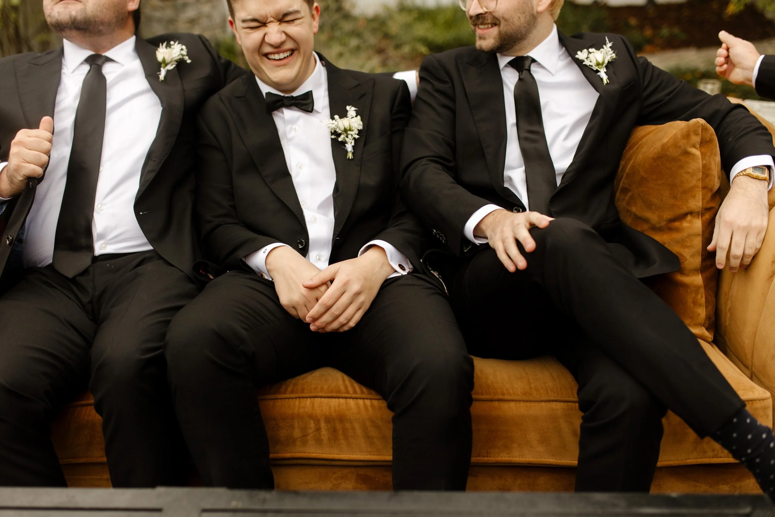 Candid close-up of the groom and groomsmen laughing together in classic black suits and tuxedos.