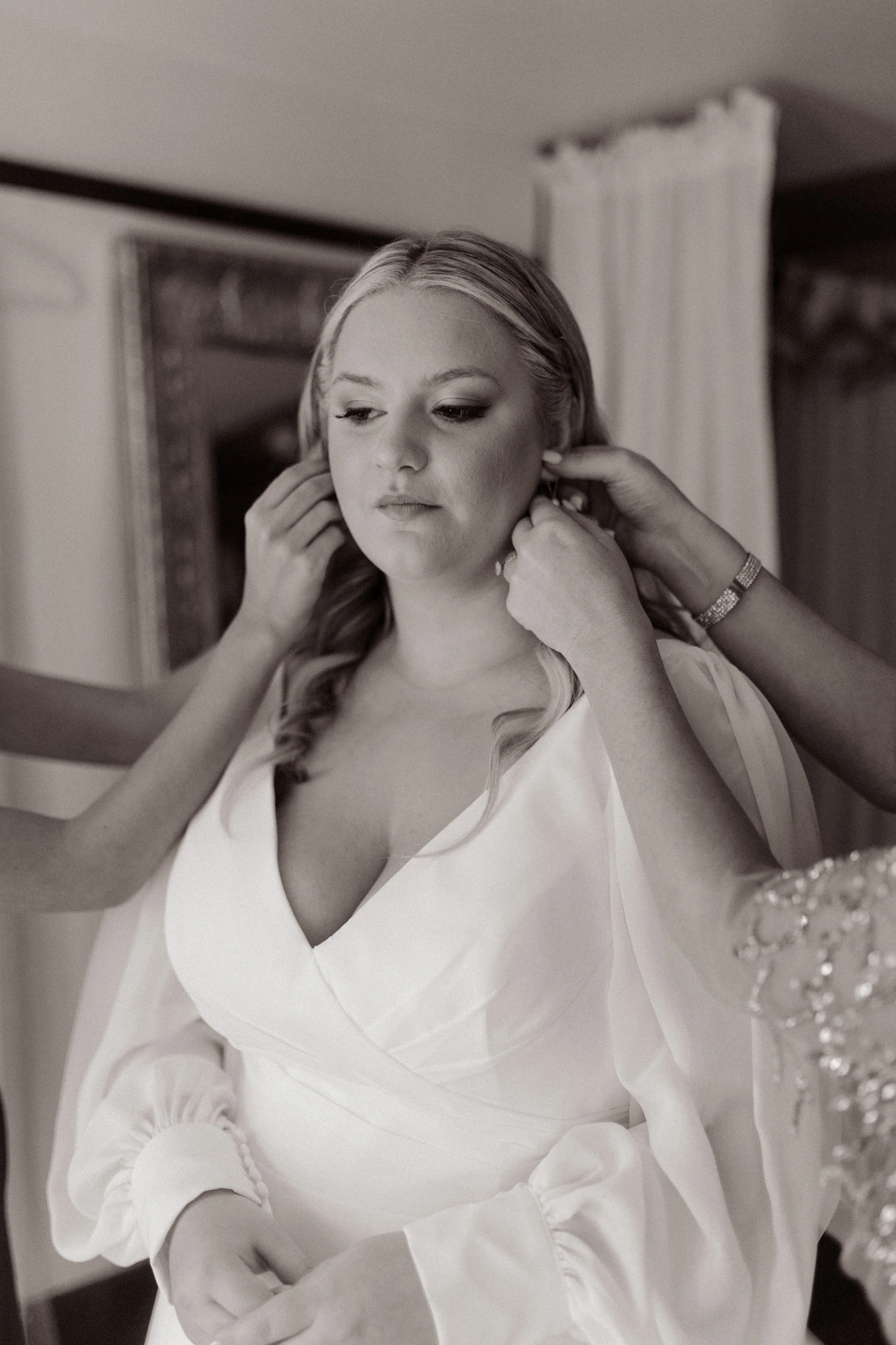 Black-and-white getting-ready photo of the bride having her earrings fastened before her fall wedding ceremony.