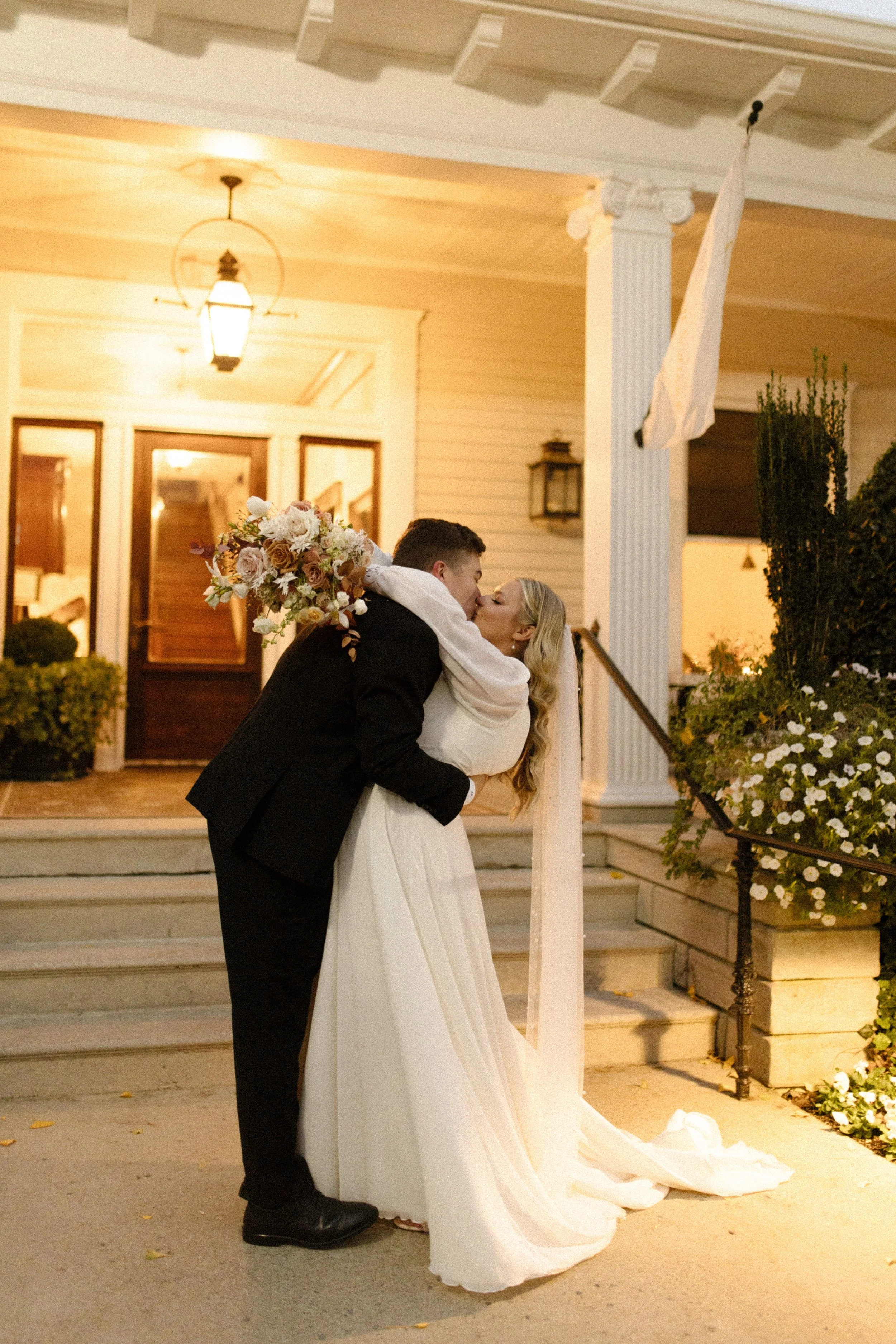 Newlyweds kissing outside the venue after their ceremony with the bride holding her peach and cream bouquet.