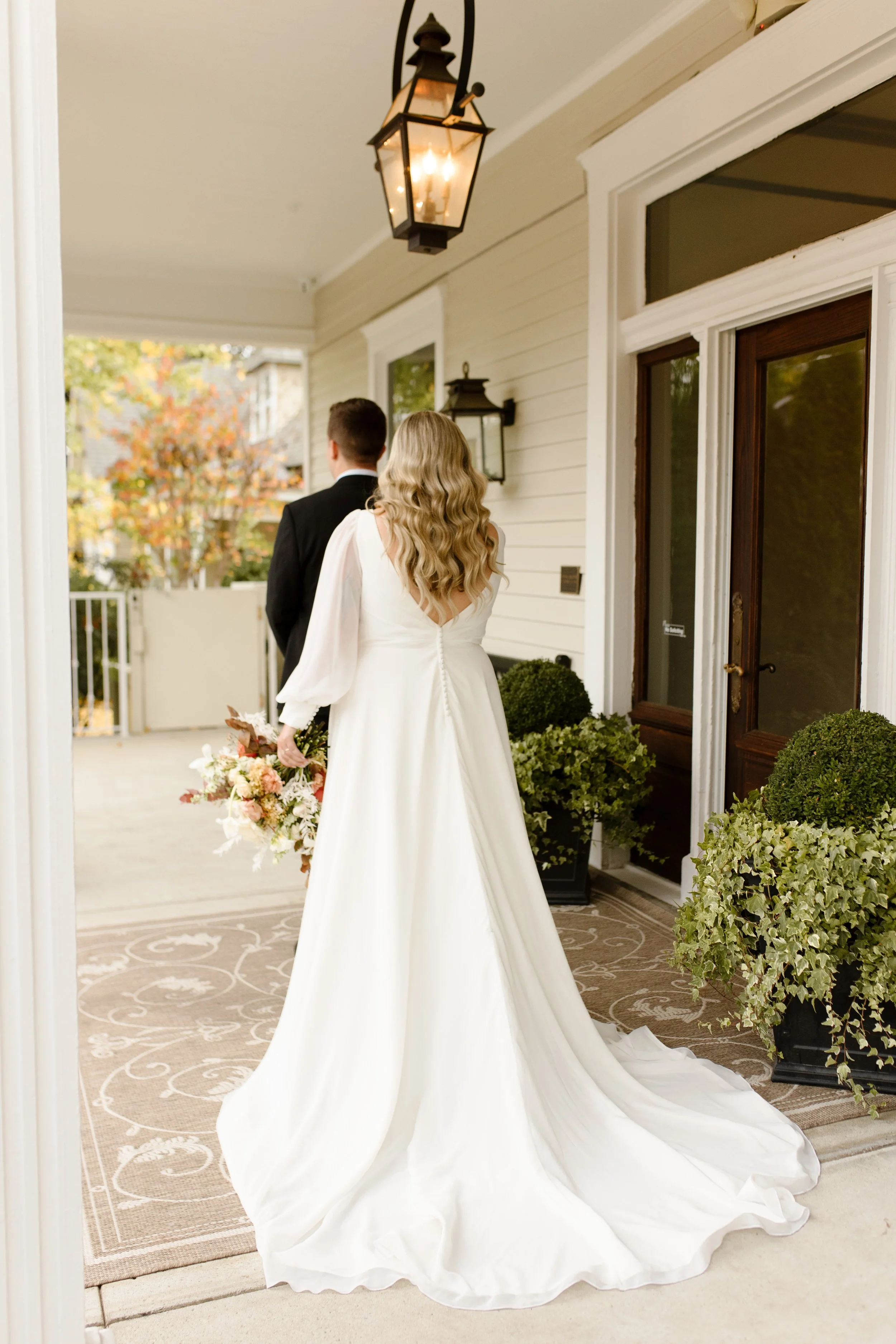 Bride walking toward the groom from behind during their first look on a covered porch.