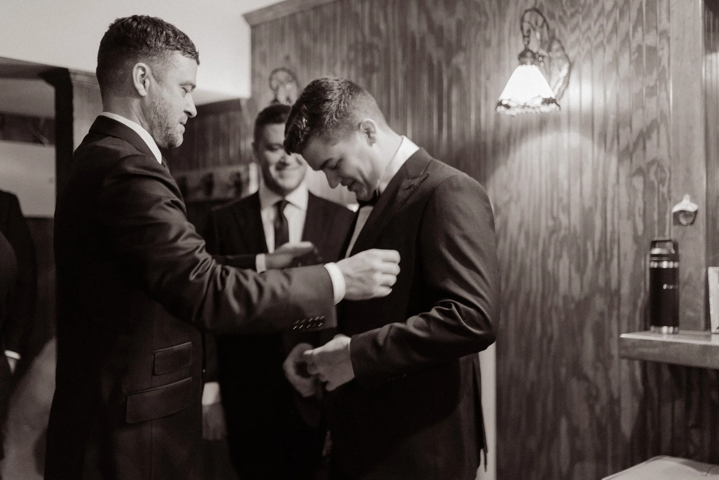 Black-and-white candid photo of the groom getting ready with his groomsmen before the ceremony.