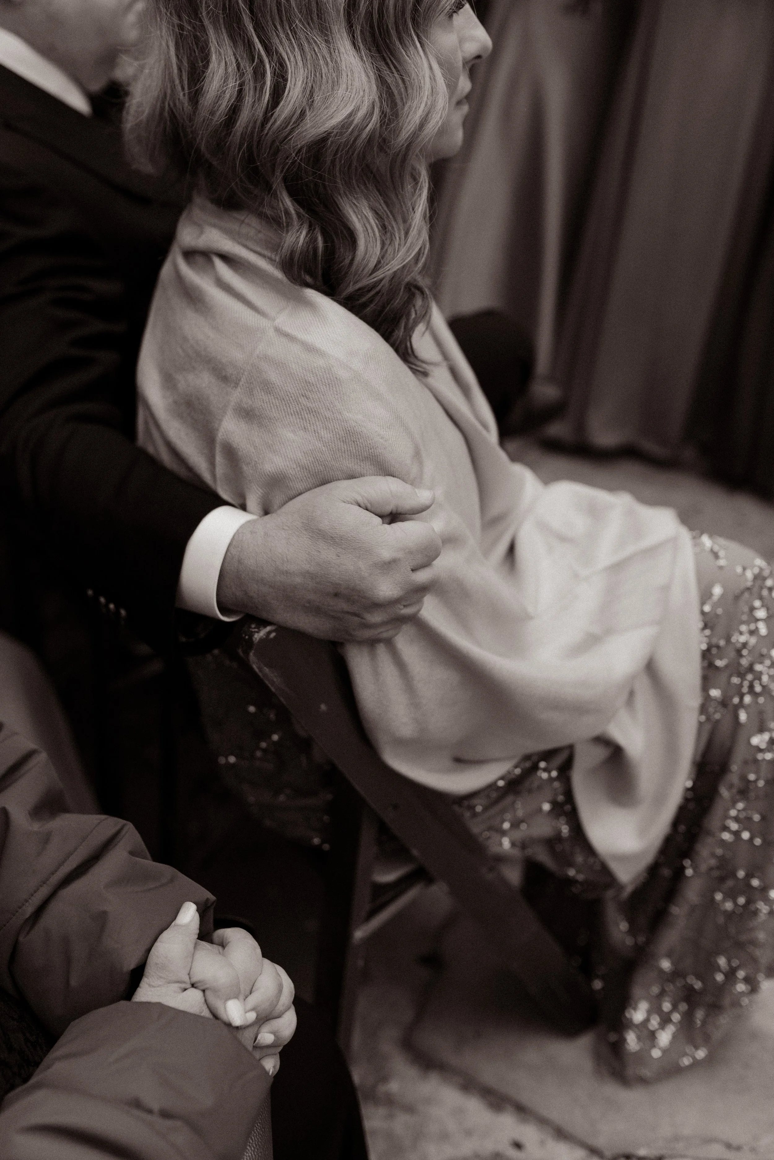 Black-and-white candid photo of wedding guests holding each other close during an emotional fall wedding ceremony.