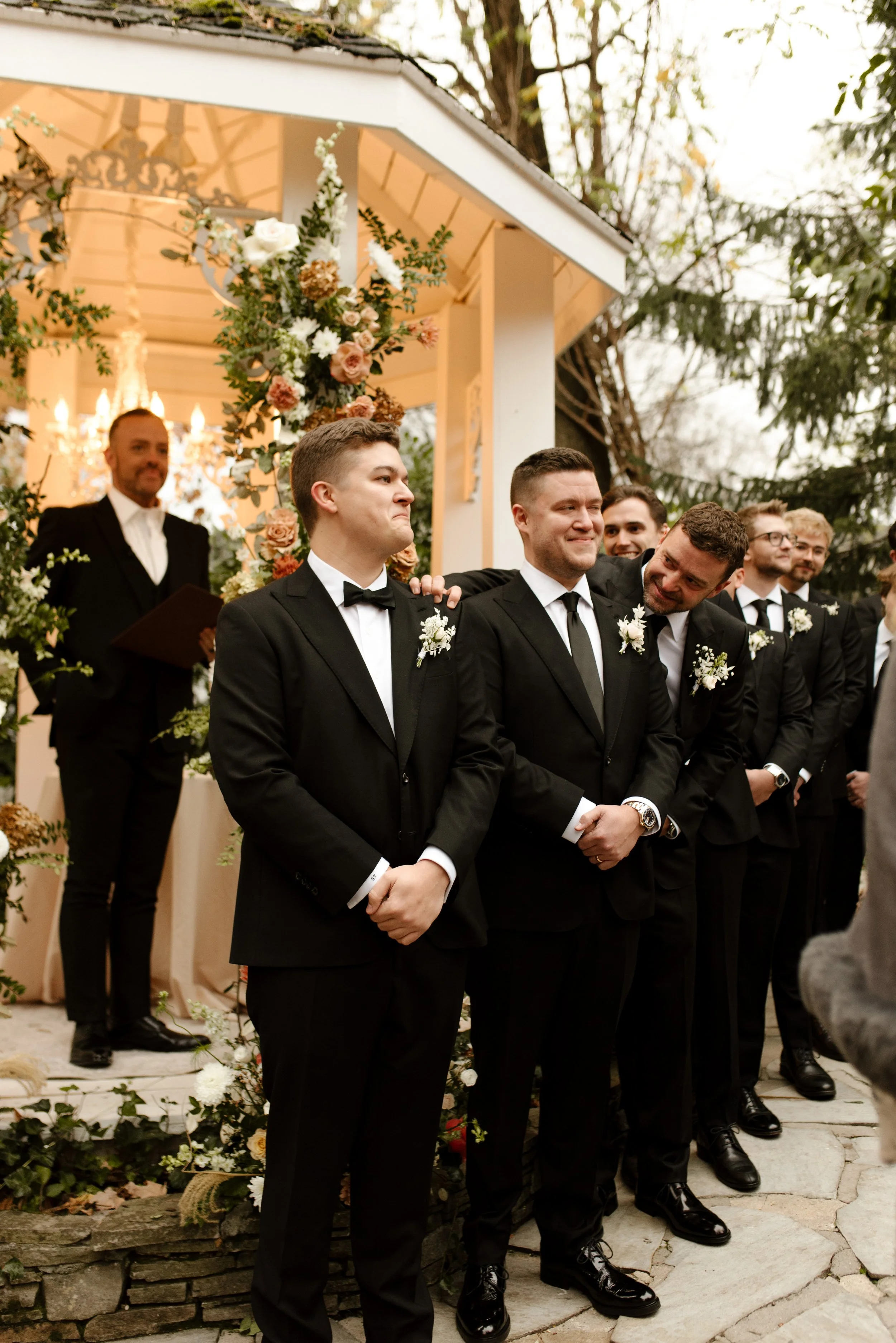 Groom standing with his groomsmen in classic black suits during an emotional outdoor wedding ceremony.