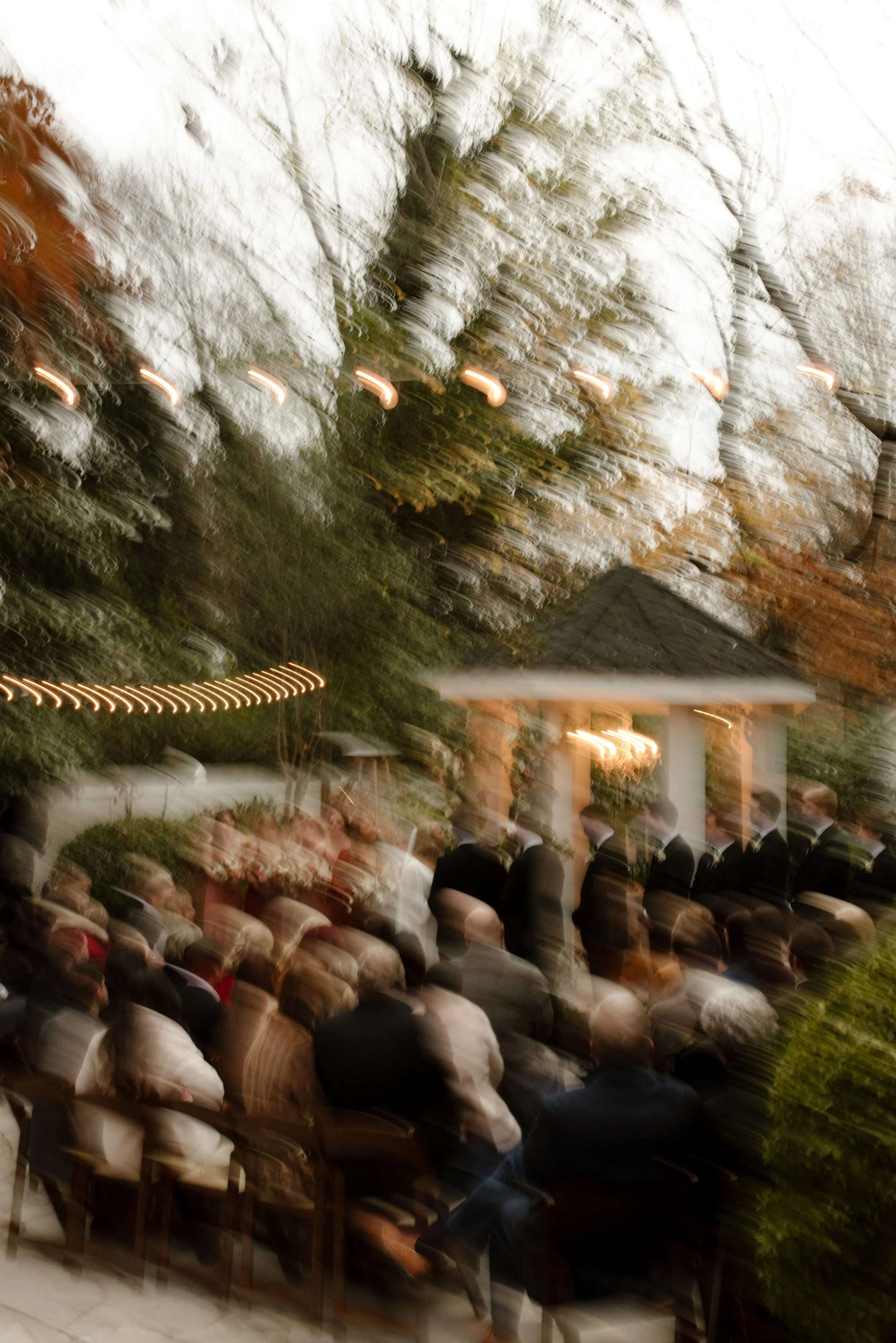 Motion-blur photo of guests gathered around a flower-covered gazebo during an outdoor fall wedding ceremony.