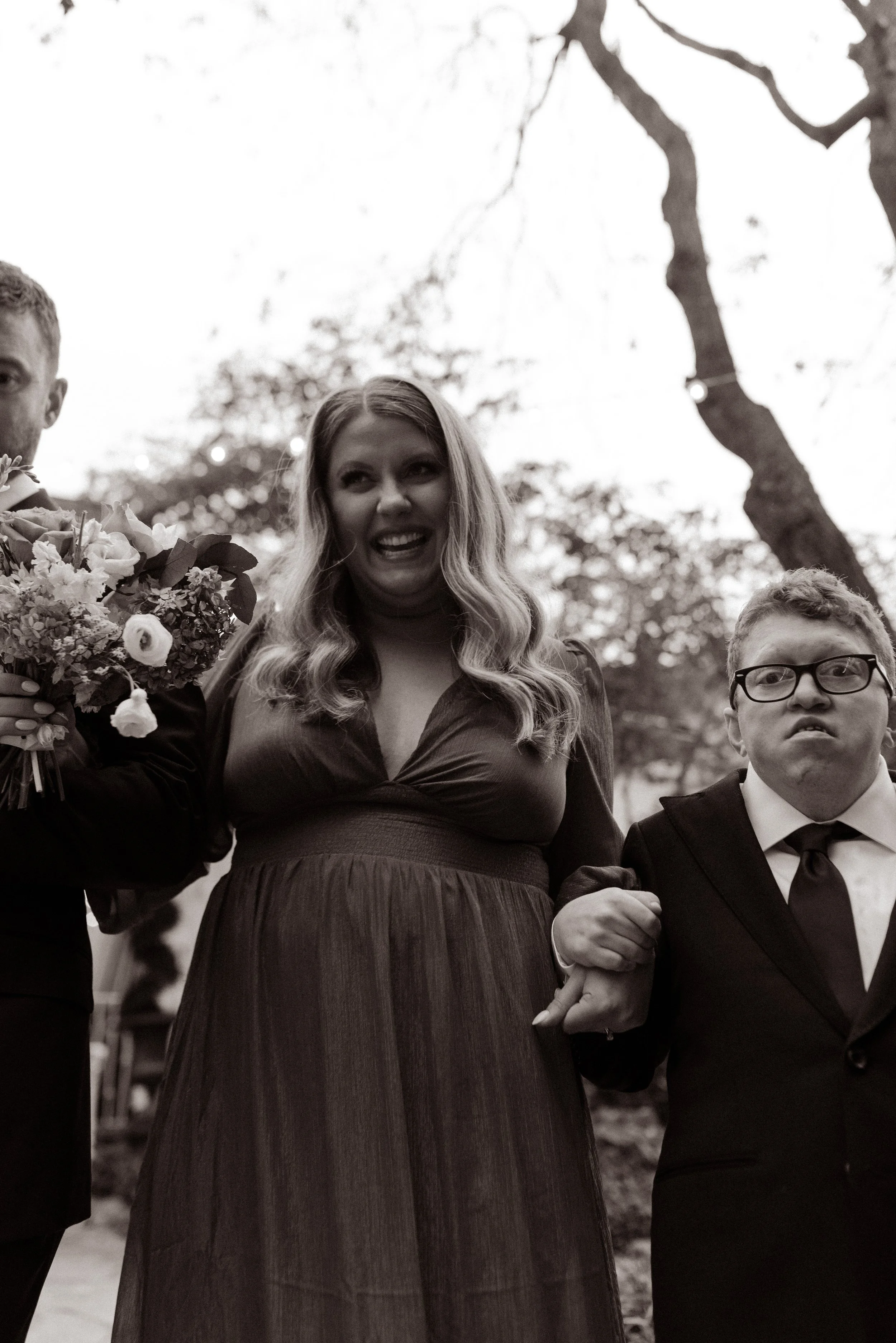Black-and-white candid photo of smiling wedding party members walking together after the outdoor ceremony.