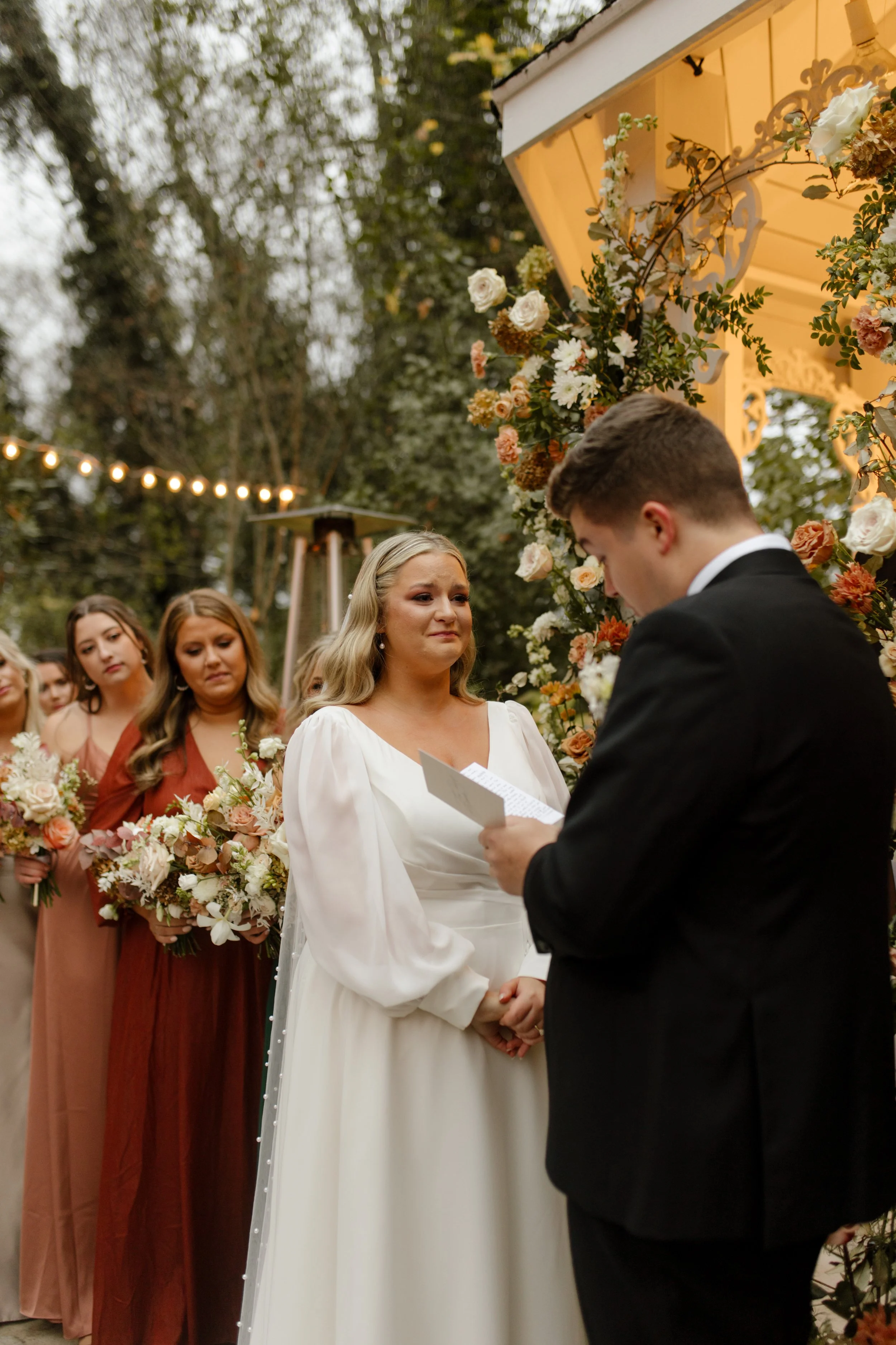 Emotional fall wedding ceremony moment as the groom reads his vows to the bride beside autumn floral arrangements.