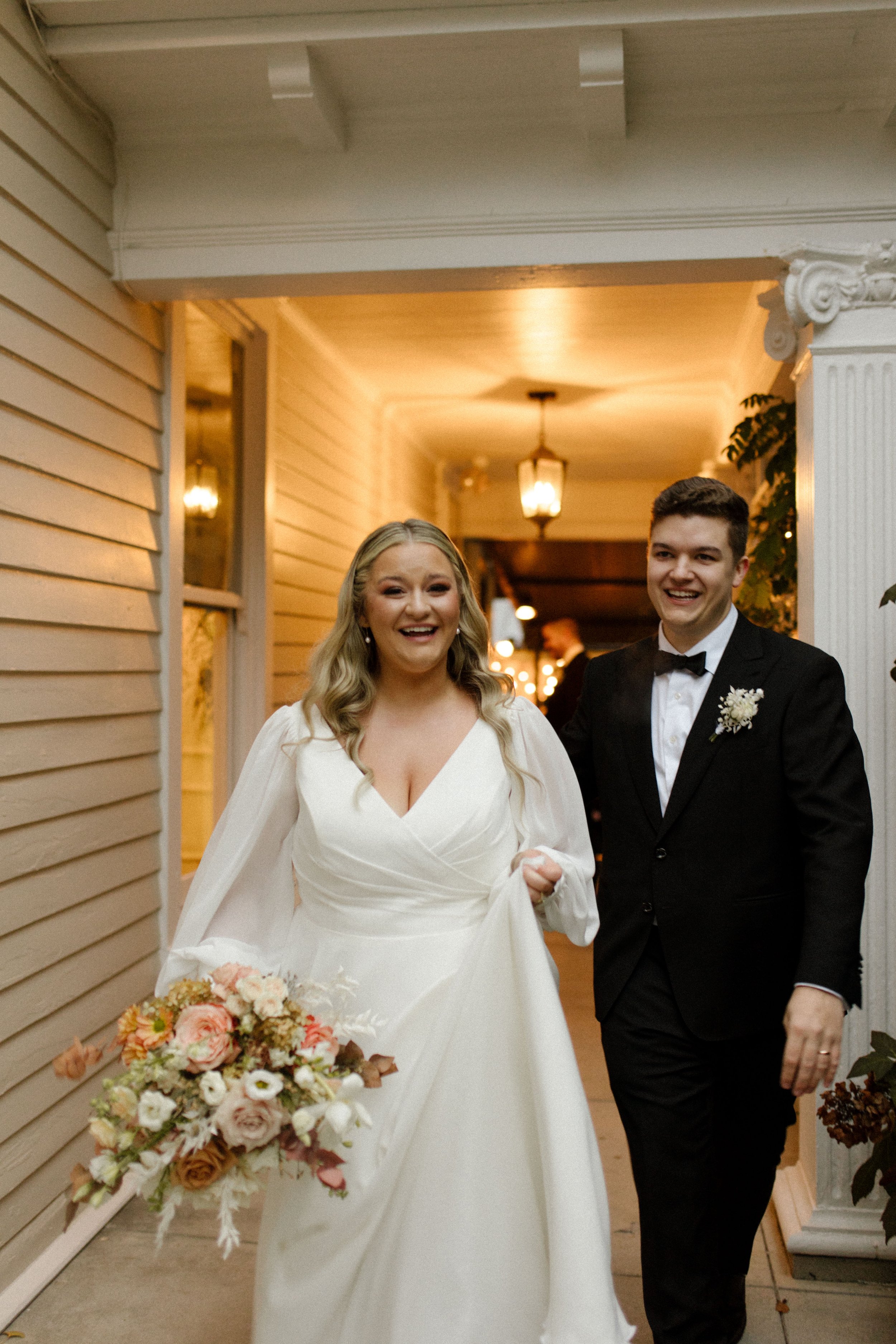 Bride and groom smiling together after their fall wedding ceremony, with the bride carrying a peach and cream autumn bouquet.