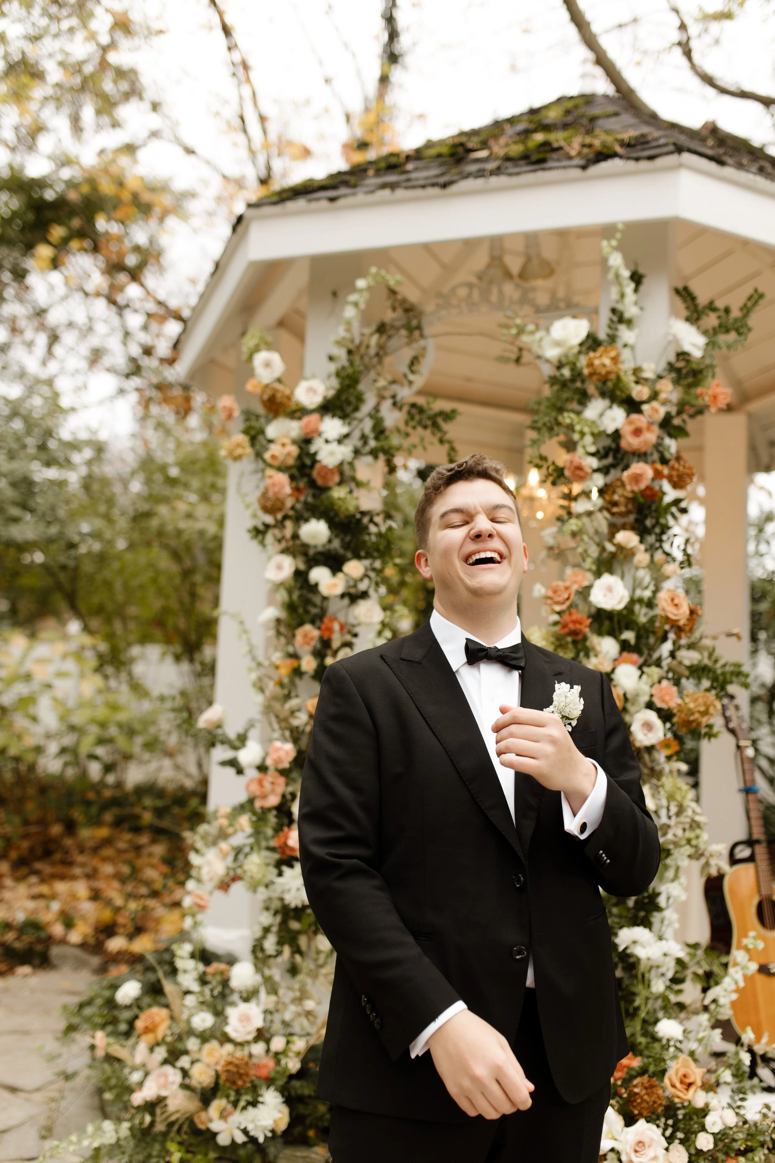 Groom laughing in front of a flower-covered outdoor gazebo before the wedding ceremony.