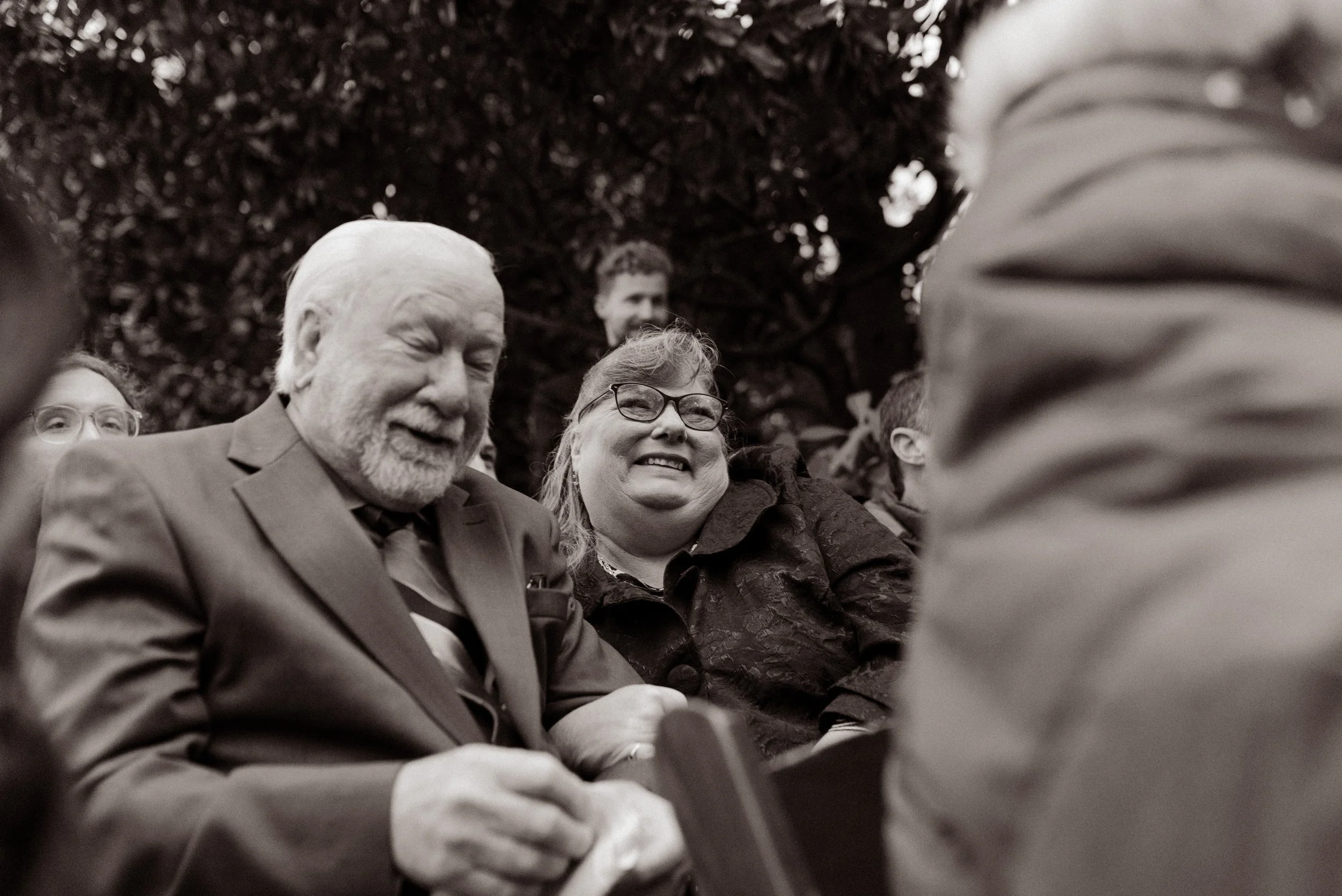Black-and-white candid photo of smiling guests bundled in coats during a chilly fall wedding ceremony.
