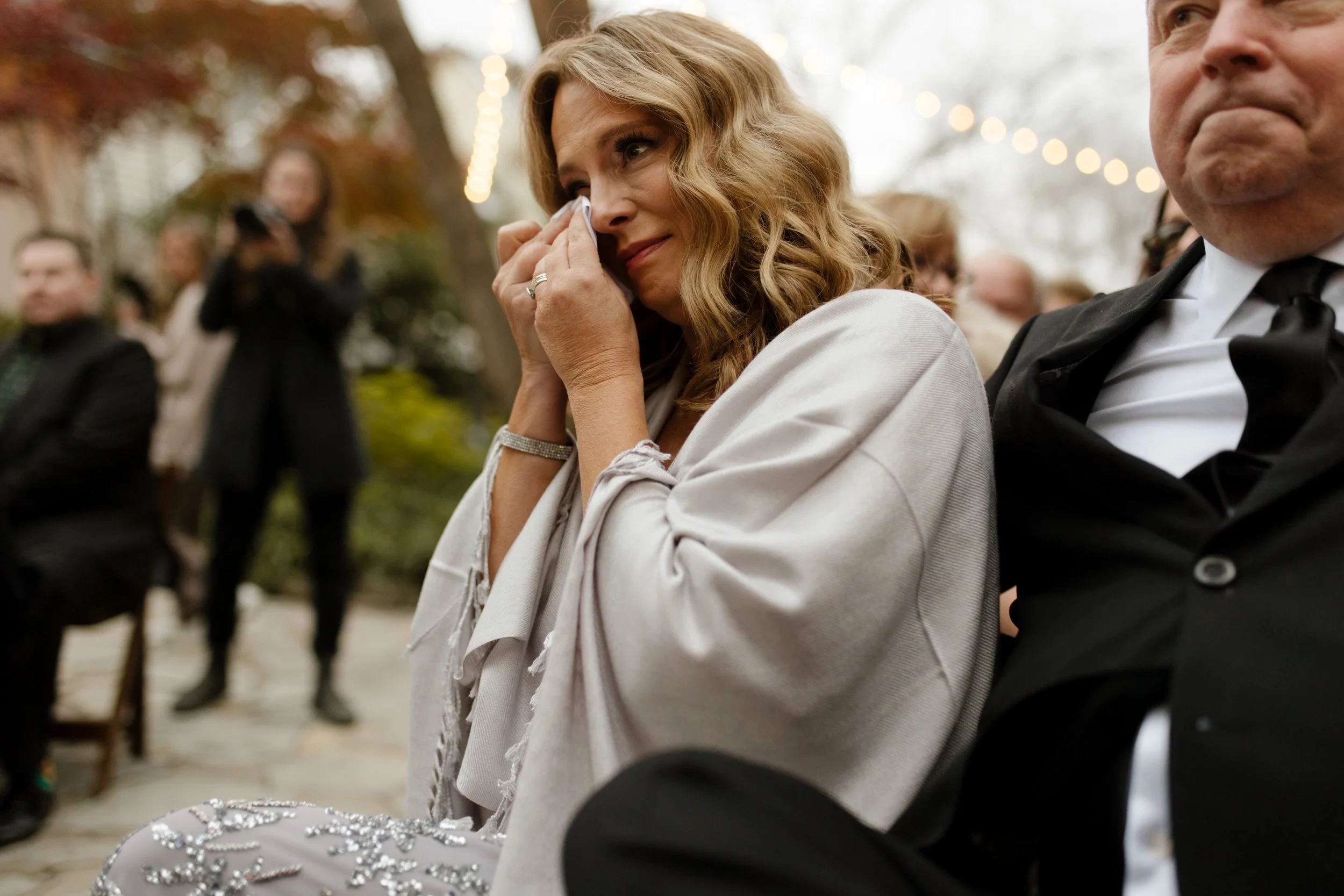 Emotional wedding guest wiping away tears while watching the outdoor ceremony.